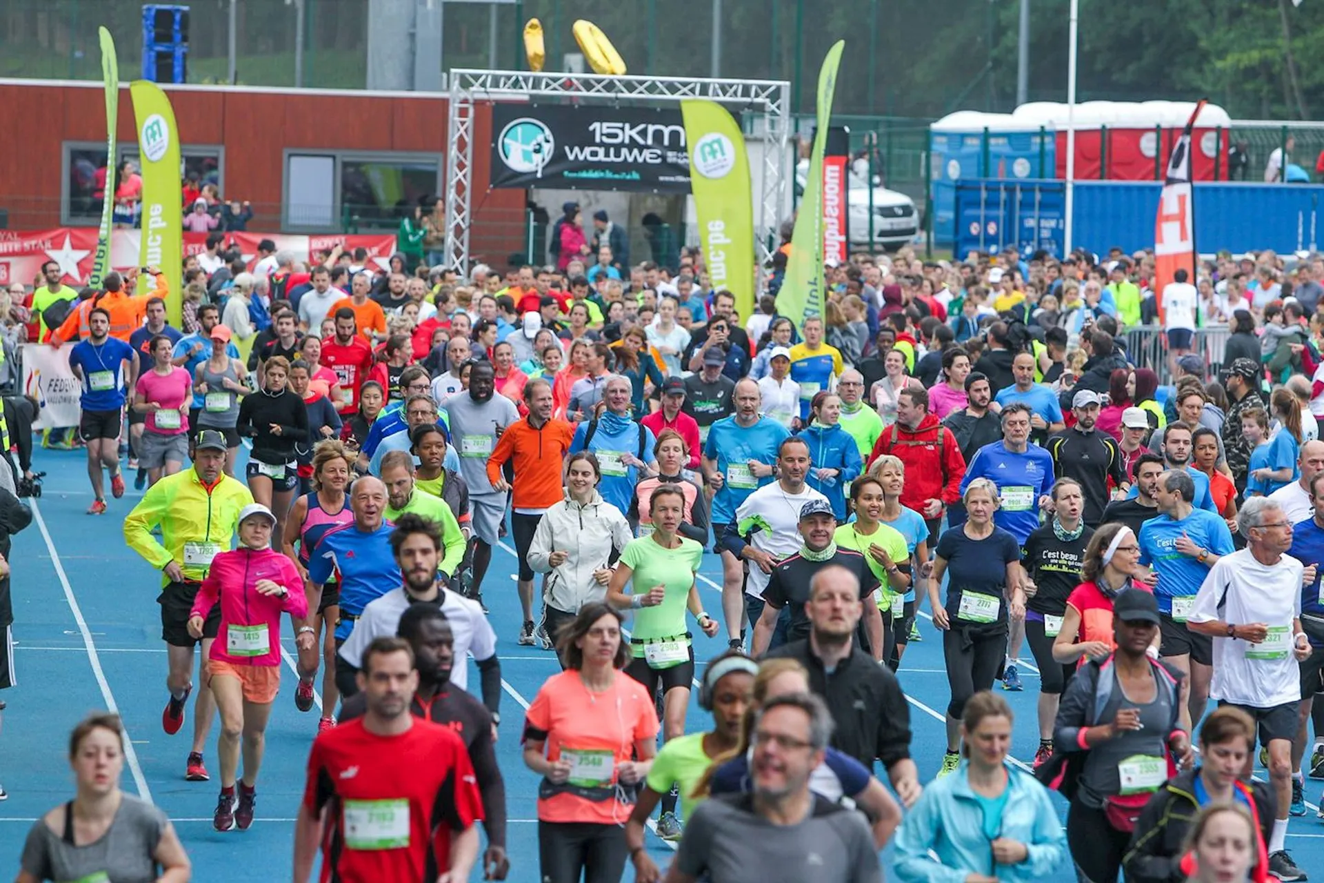 The image shows a large group of runners at the start of a road race.