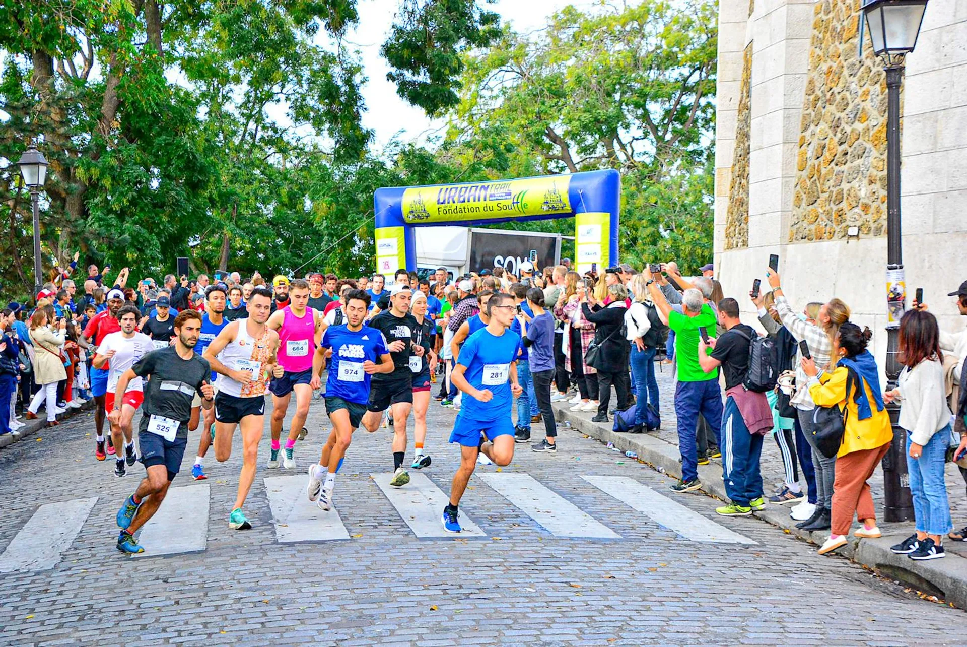 The image depicts a group of runners at the start of a road race. They