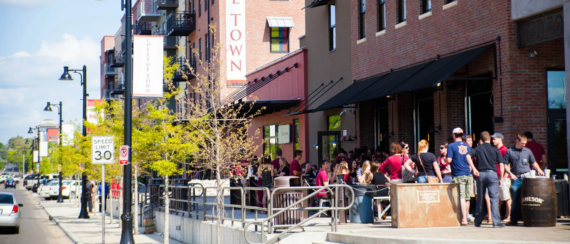 The image depicts a lively urban street scene. There is a crowd of people gathered