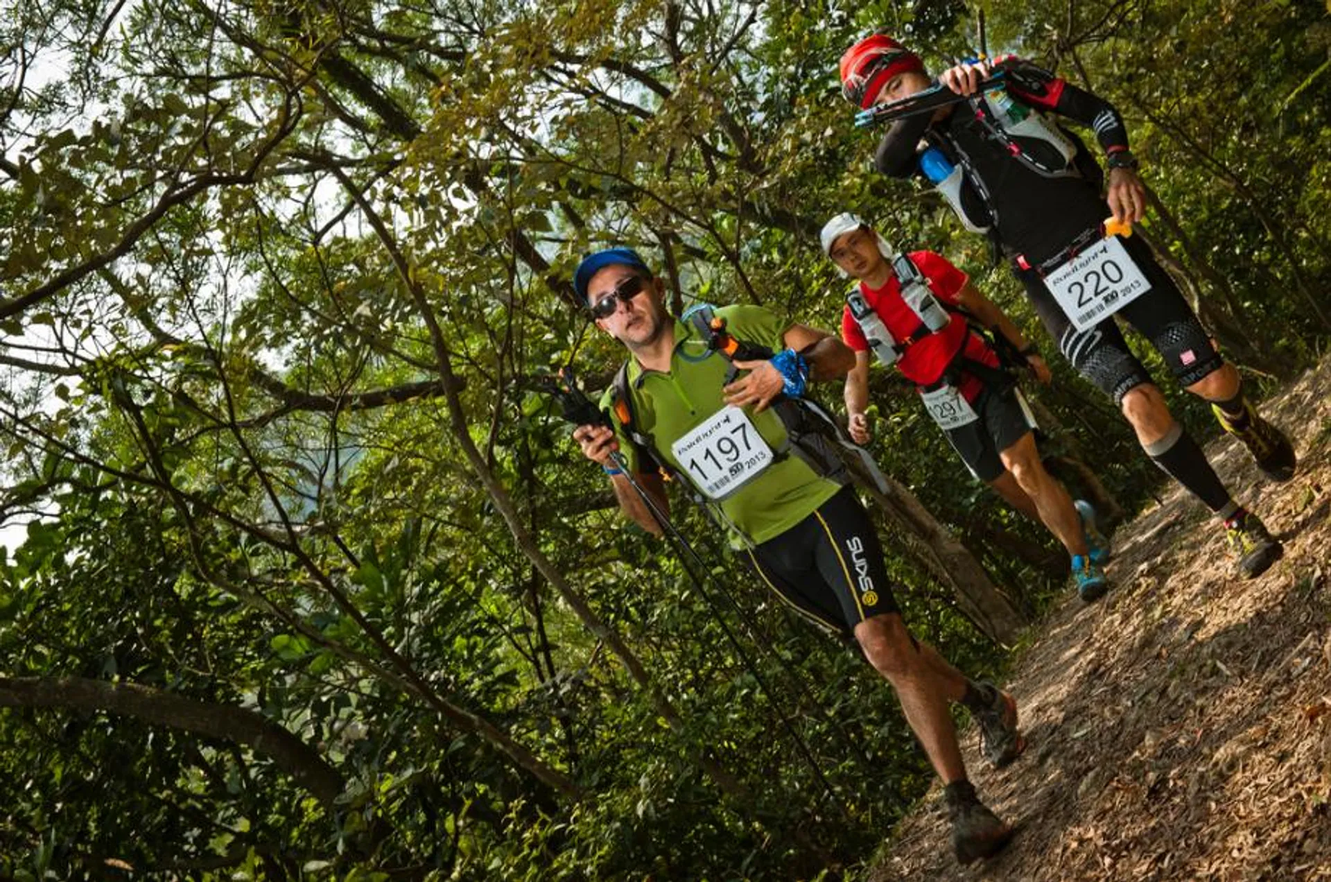 The image shows a group of three trail runners or adventure racers moving through a
