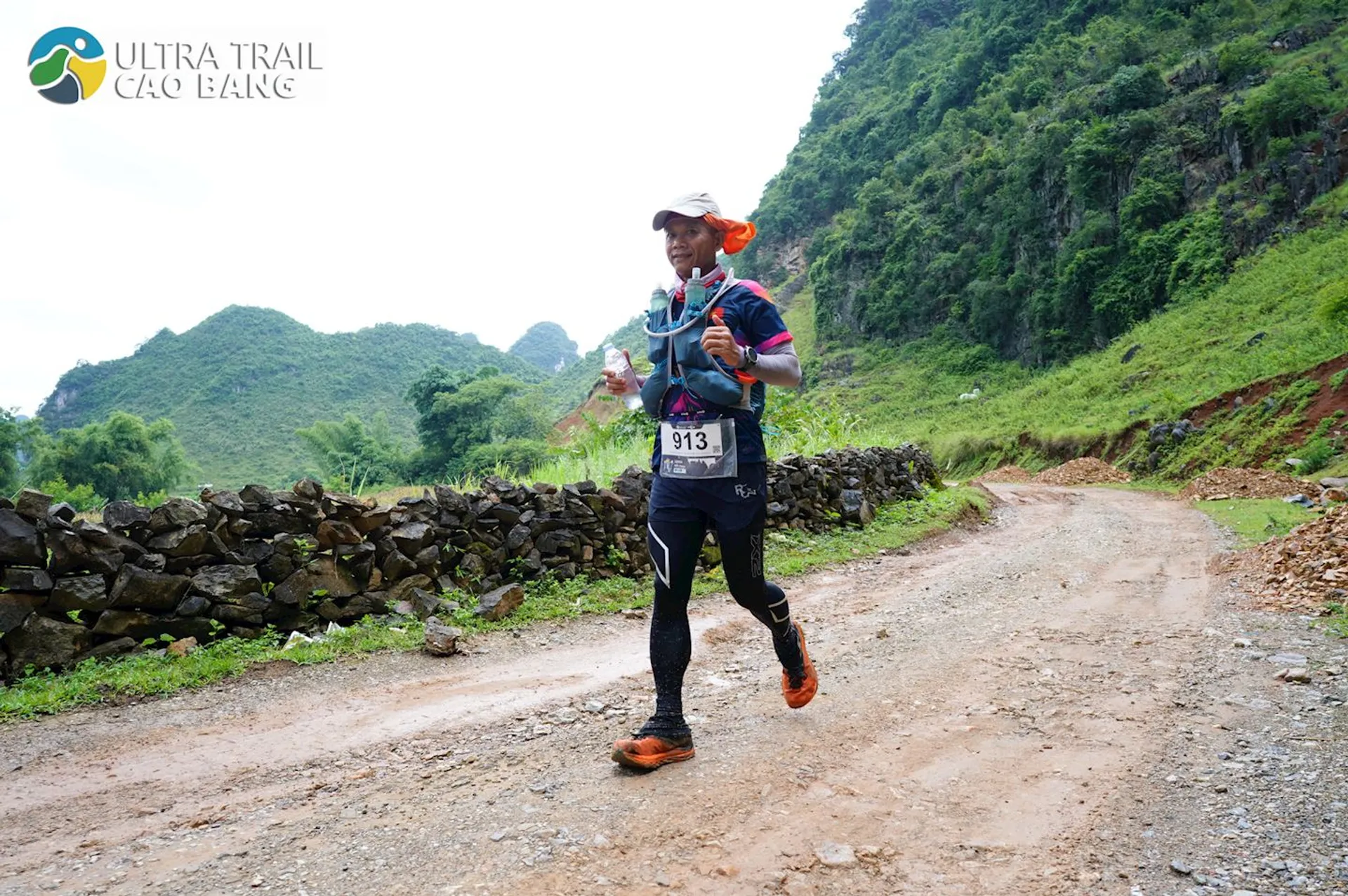 The image shows a participant in a trail running event. The runner is dressed in