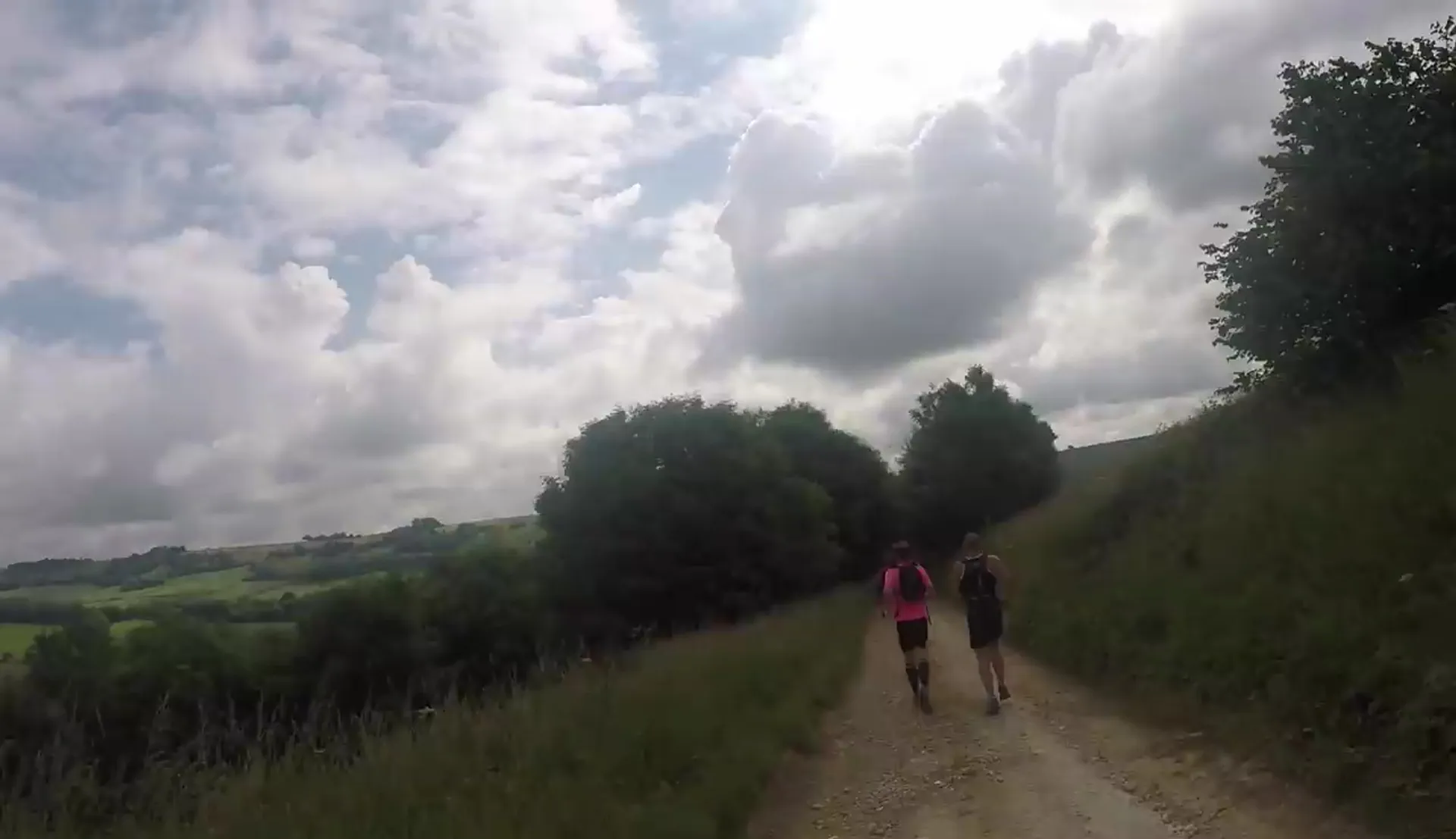 The image shows two individuals walking along a dirt path or trail in a rural or