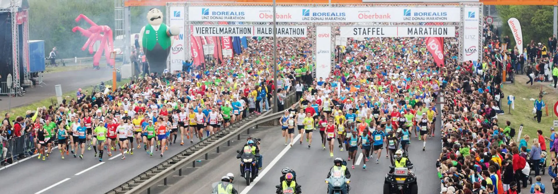 This image features a large crowd of runners at the start of a marathon or running