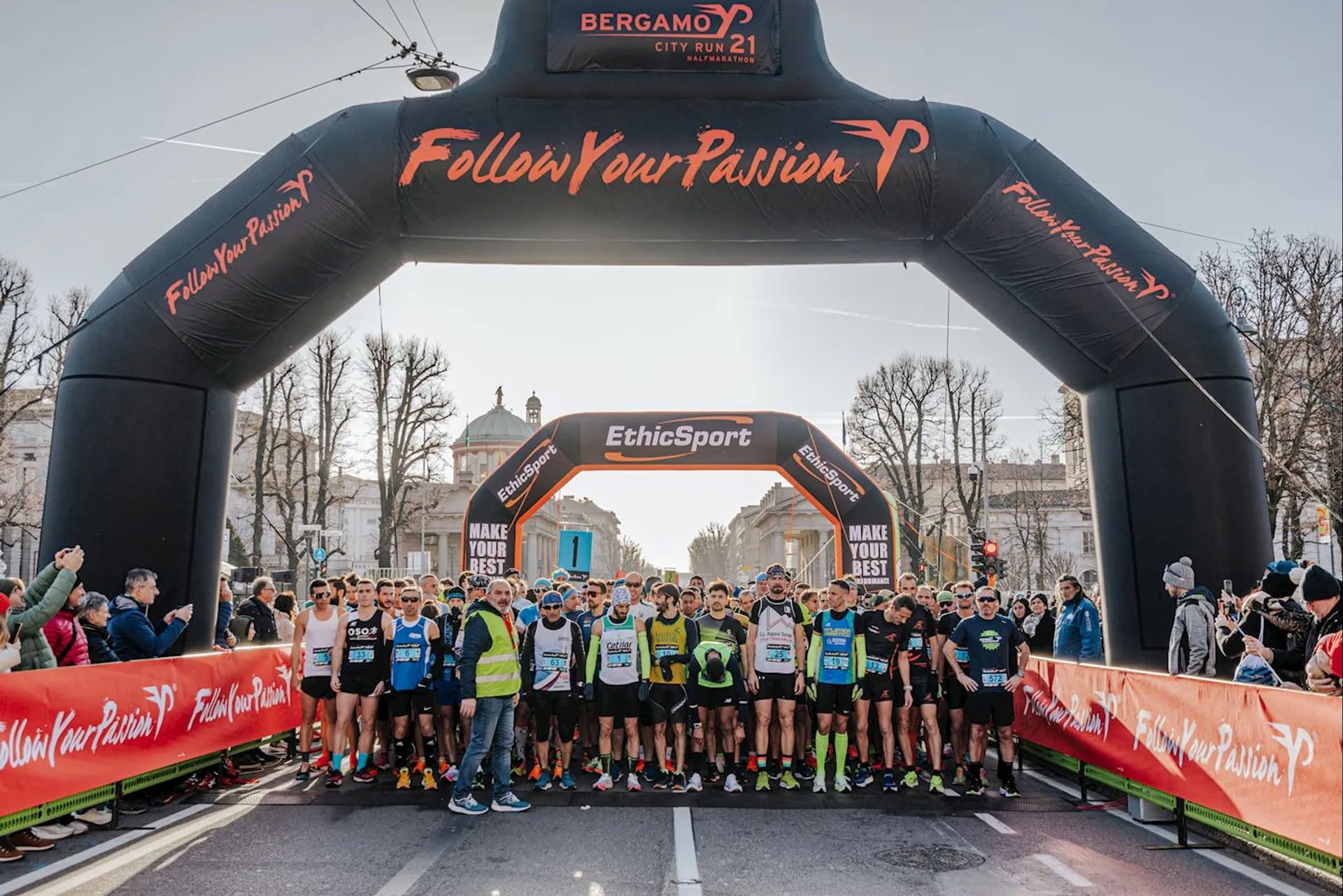 The image shows a group of runners lined up at the start line of a road