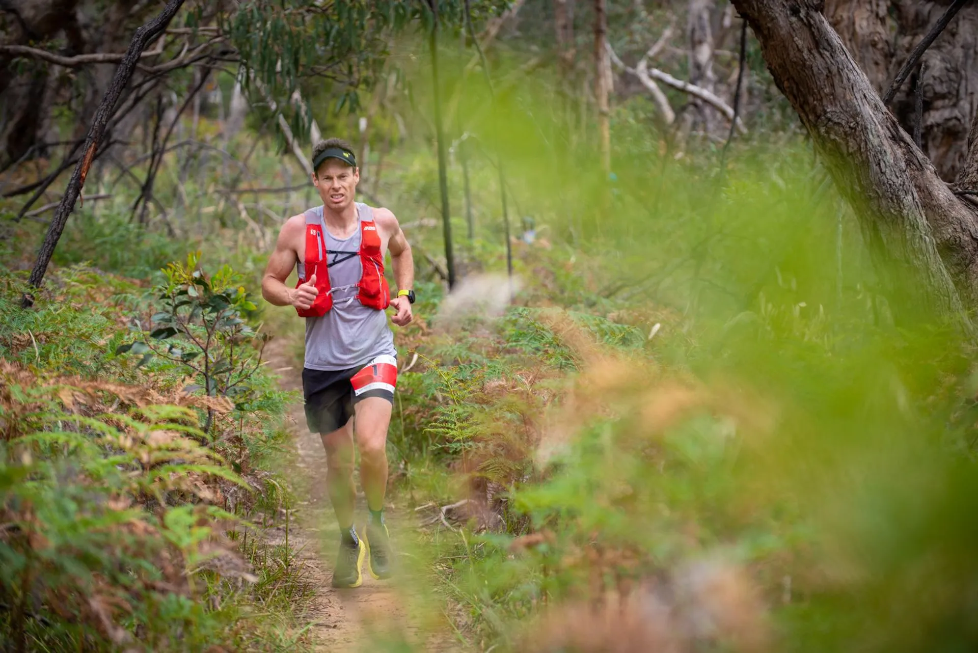 The image depicts a person trail running through a natural, wooded area. The runner