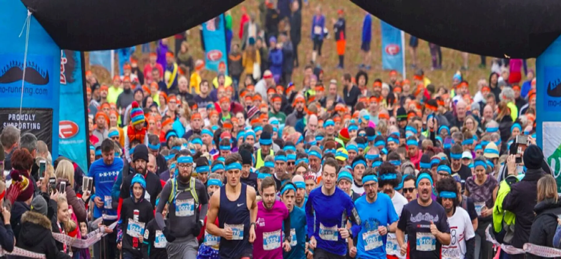 The image shows a large group of runners at the starting line of a race,
