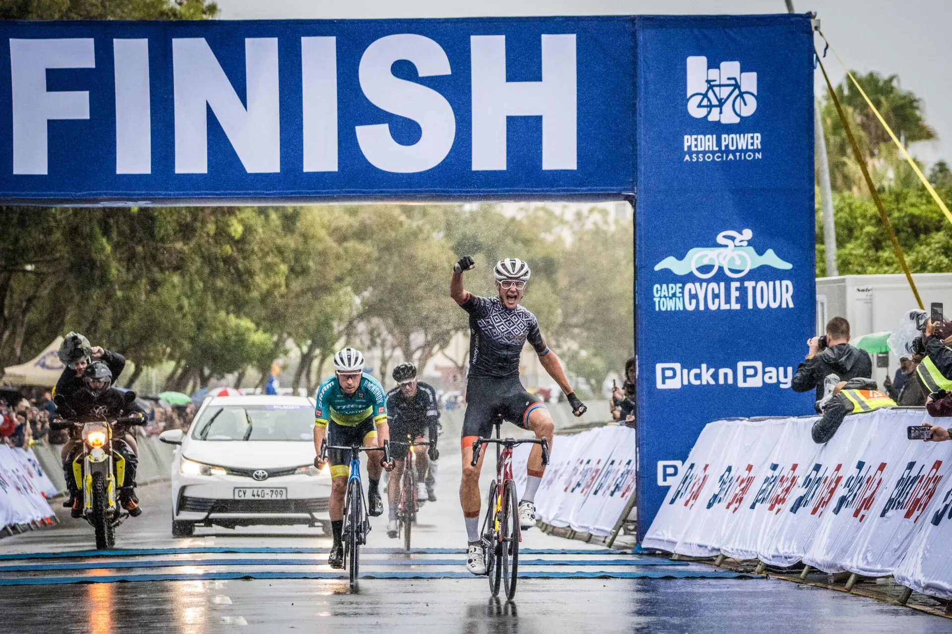 This image depicts a cycling race finish line. Several cyclists are crossing the finish line