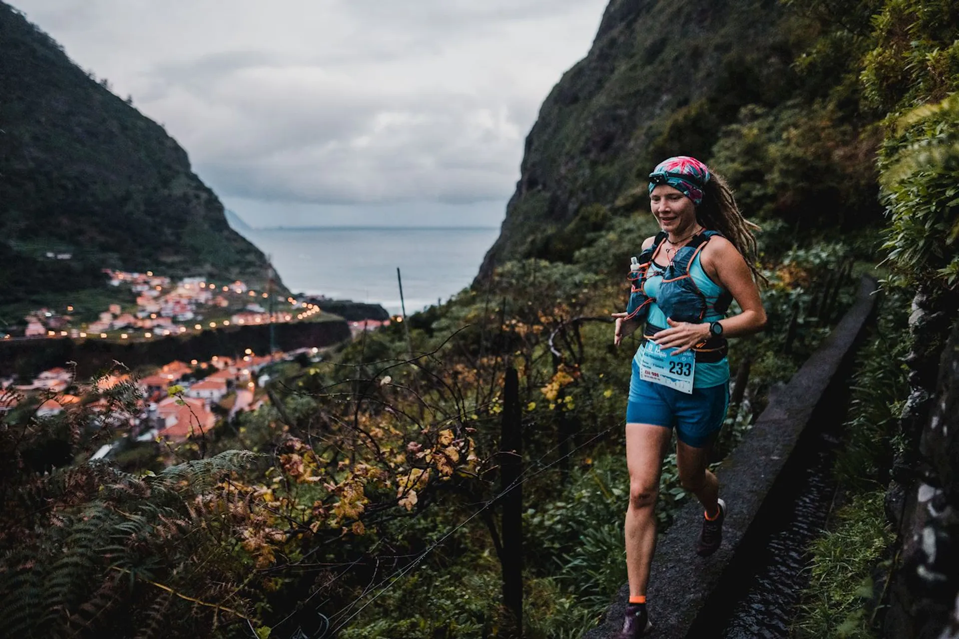 The image shows a female trail runner in motion, wearing a blue tank top,