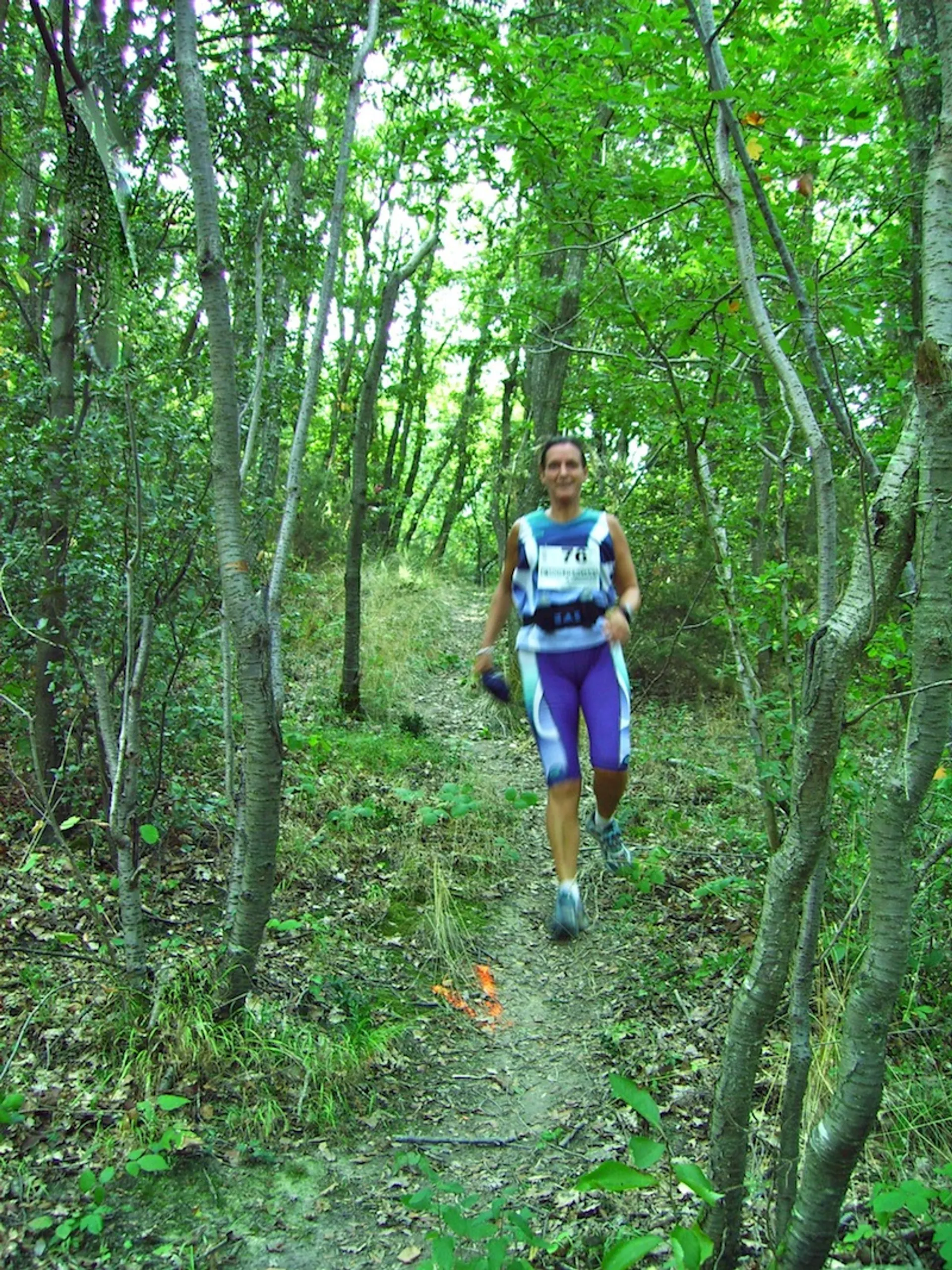The image shows a person engaged in trail running or hiking in a wooded area.