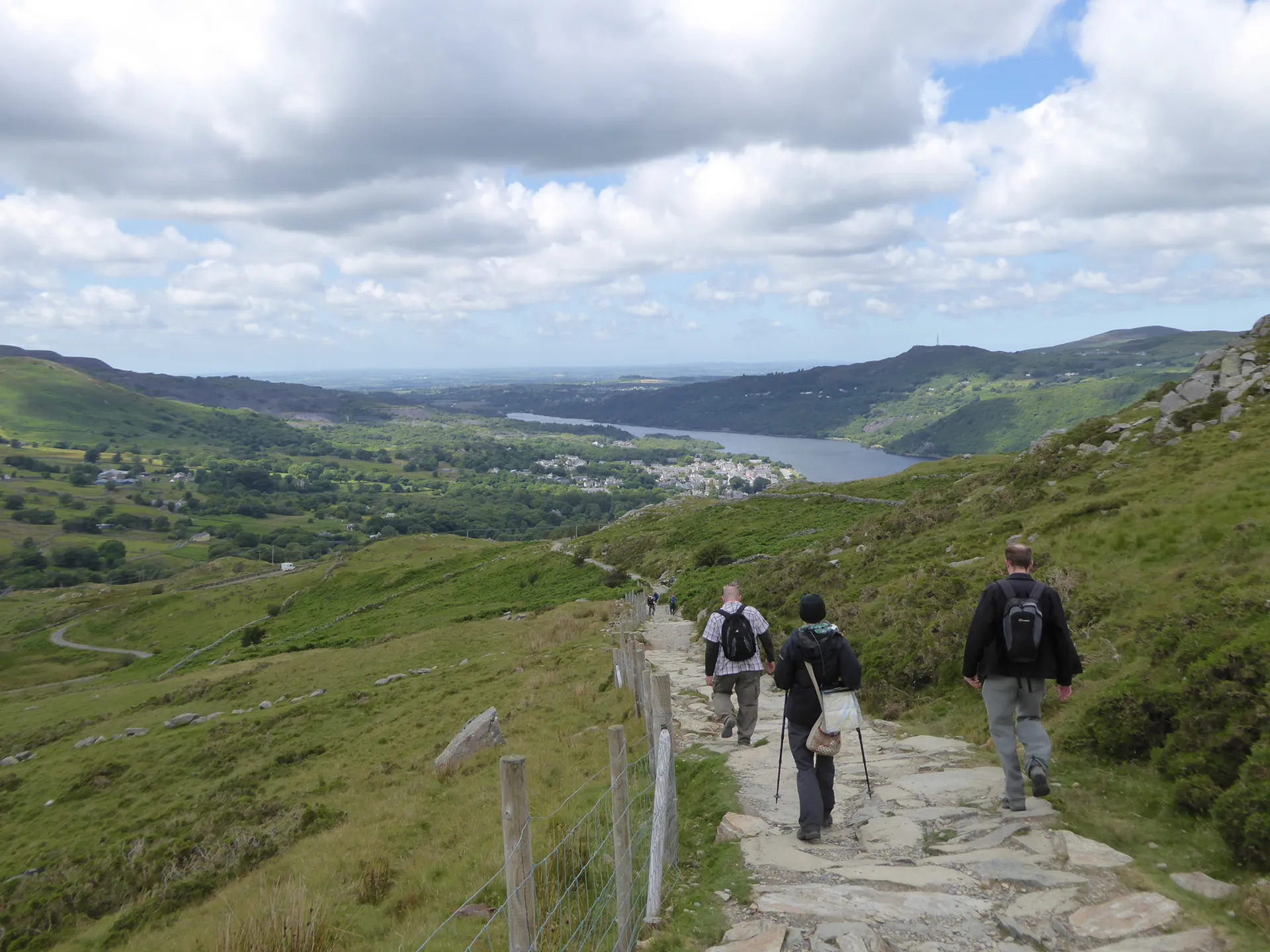The image shows three individuals hiking a trail with backpacks. They are walking on