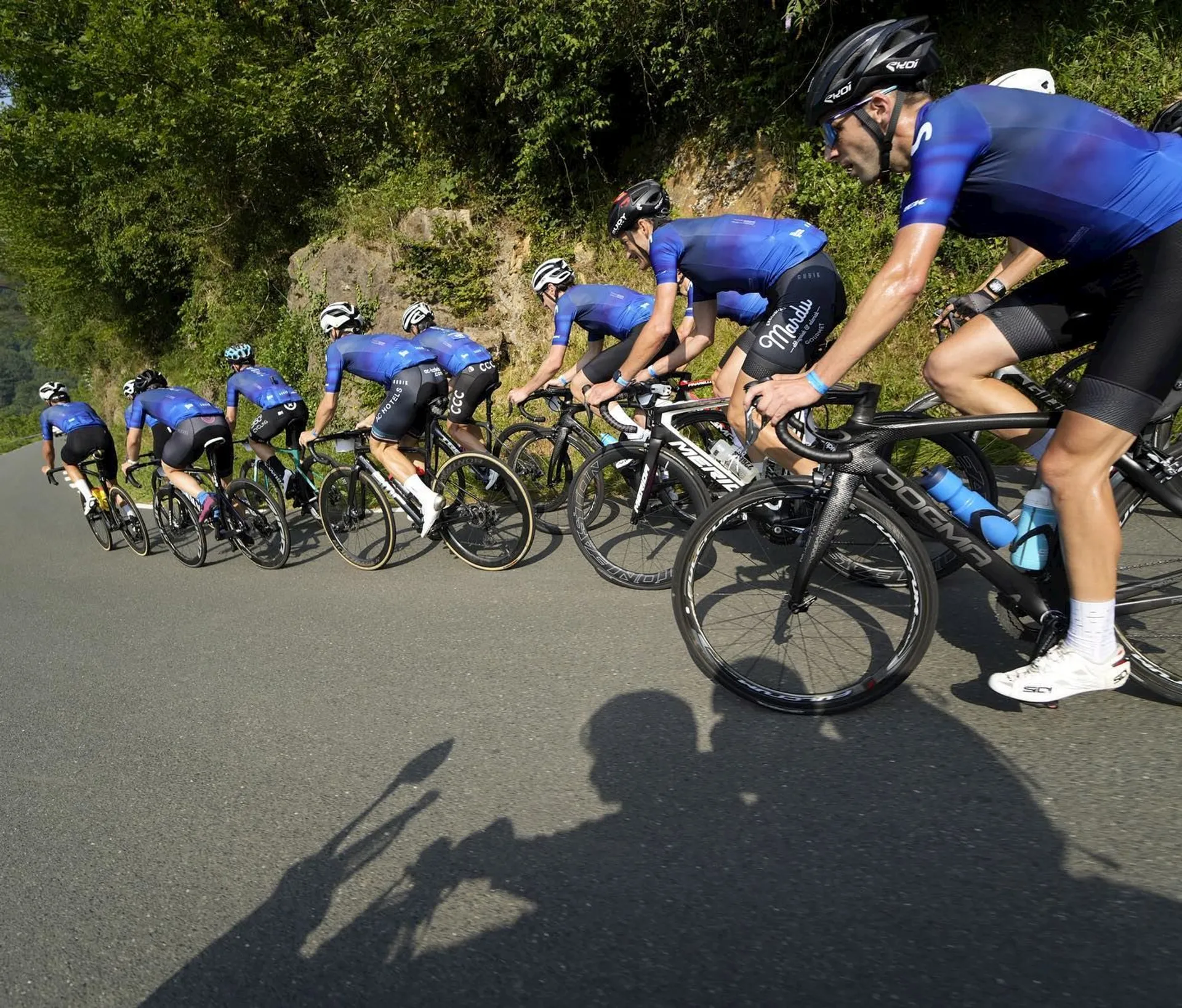 The image shows a group of cyclists in racing attire, riding in close formation on