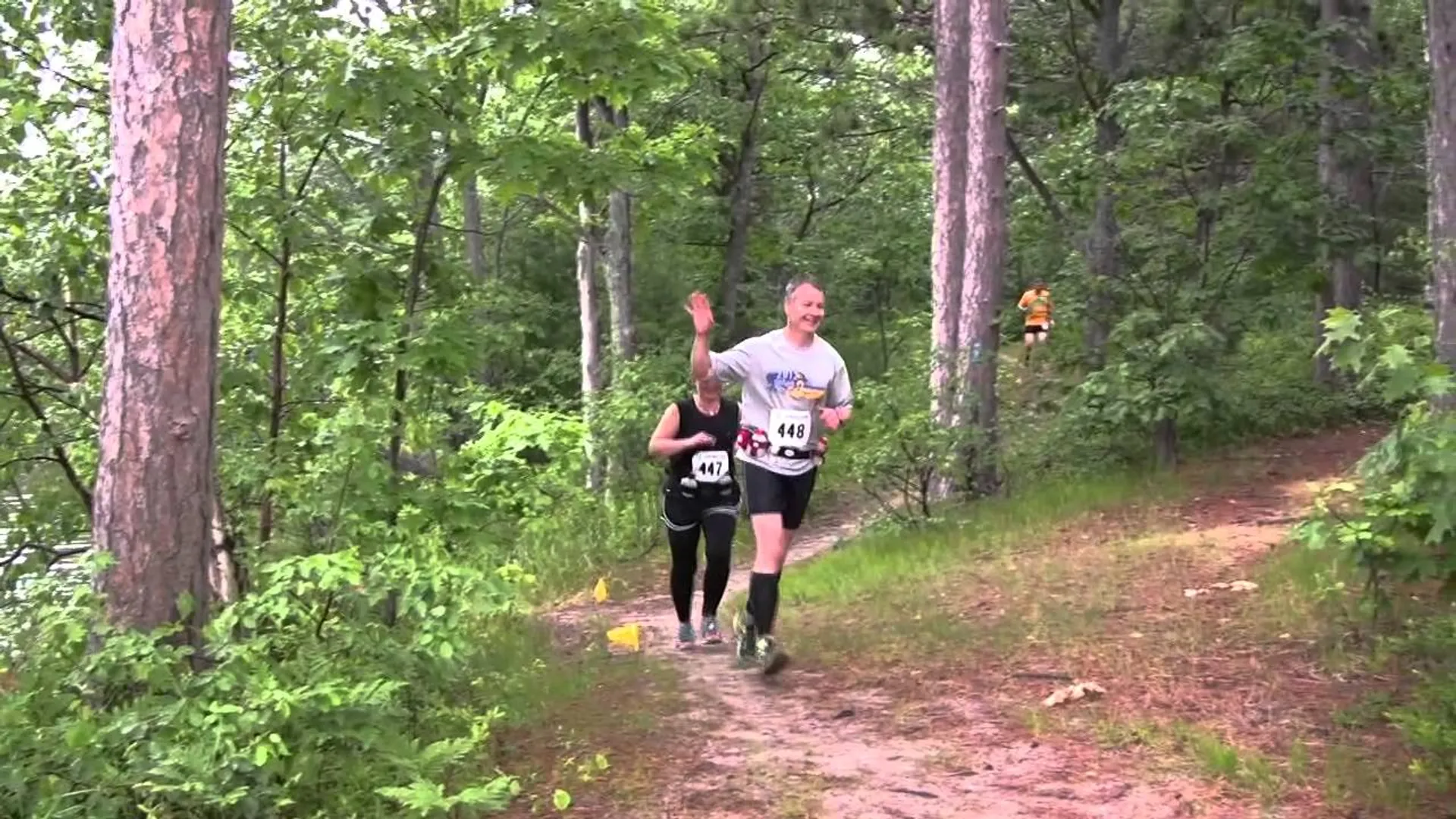 The image shows two people engaged in trail running through a wooded area. They appear