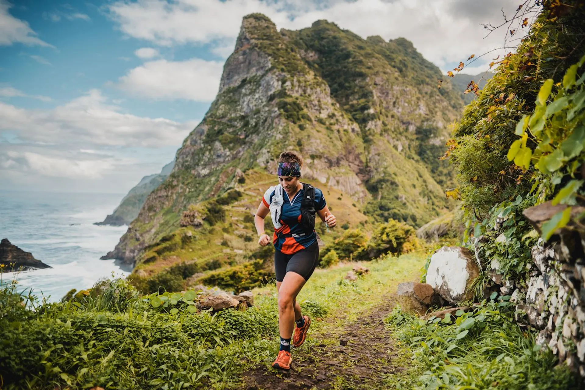 The image shows a person trail running along a narrow dirt path. The surroundings are