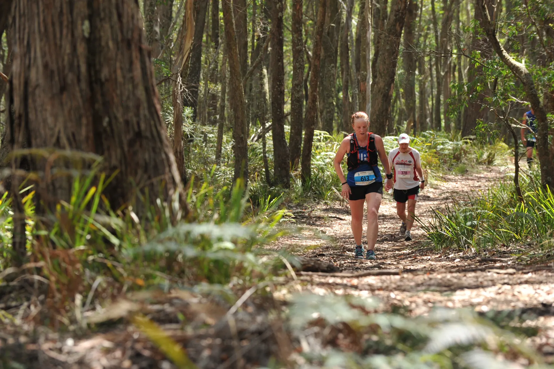 The image shows two runners in a natural, forested setting, participating in what
