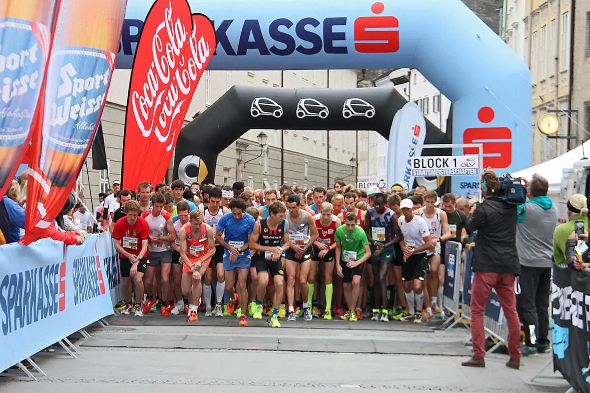 The image shows a group of runners lined up at the start line of a race