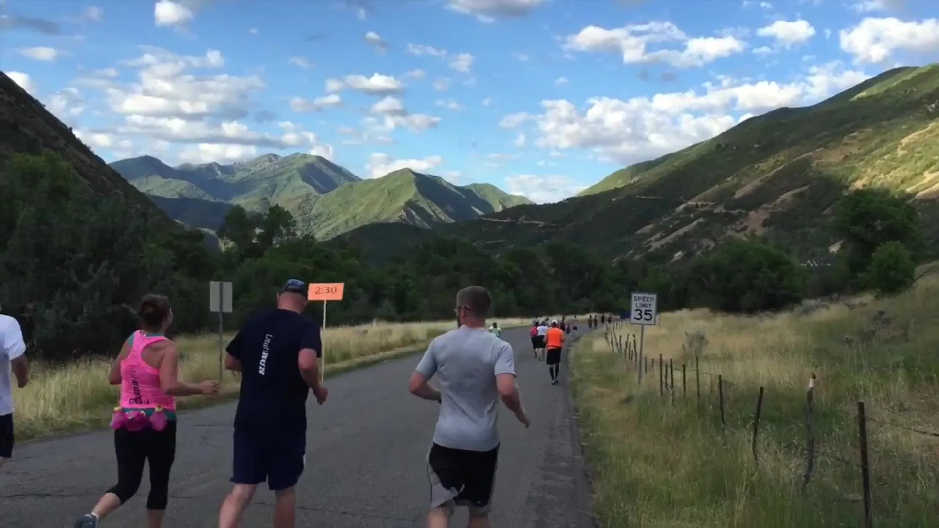 The image shows a group of people running or jogging along a road with a backdrop