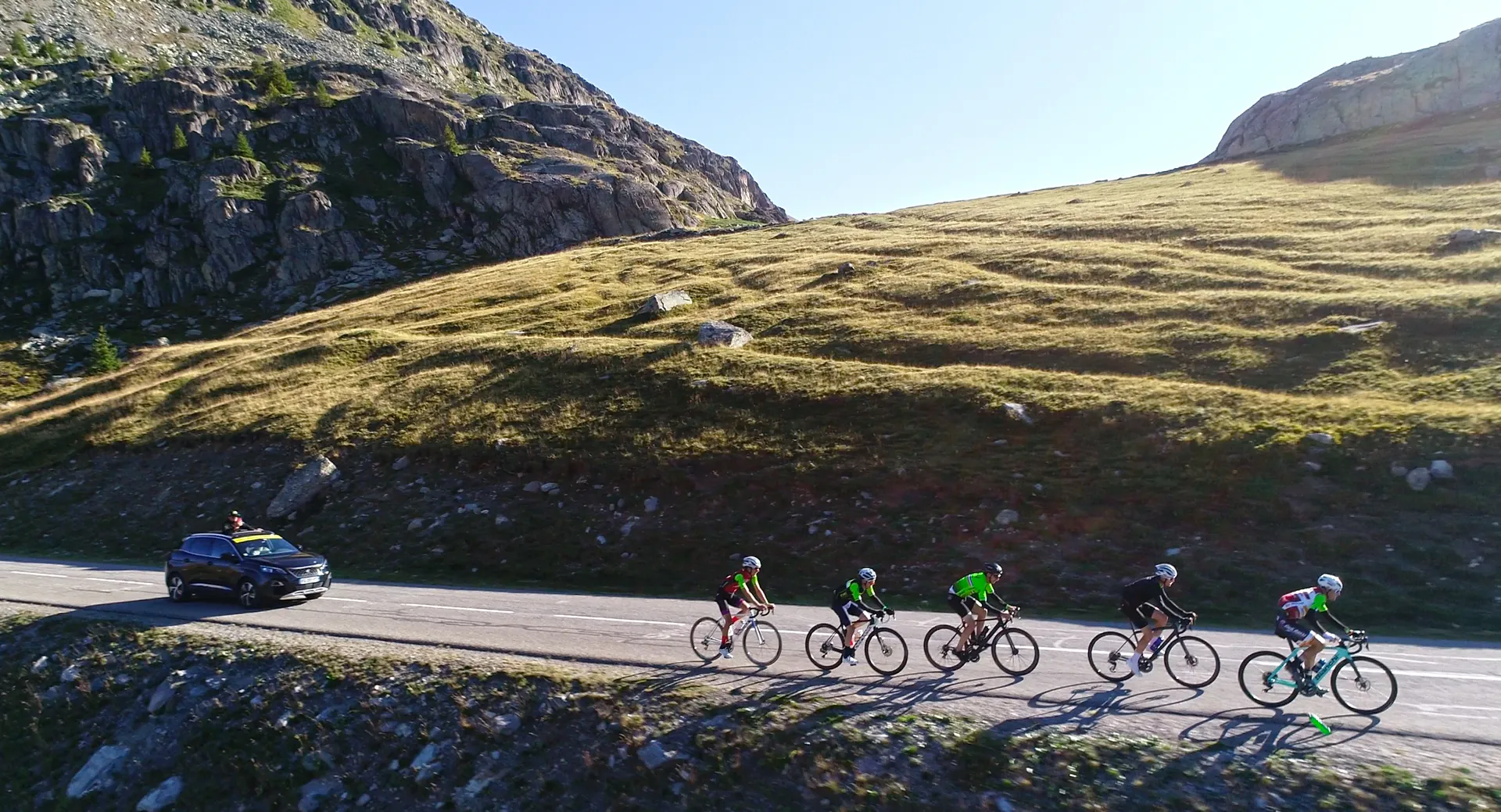 The image shows a group of cyclists riding along a road in a mountainous region