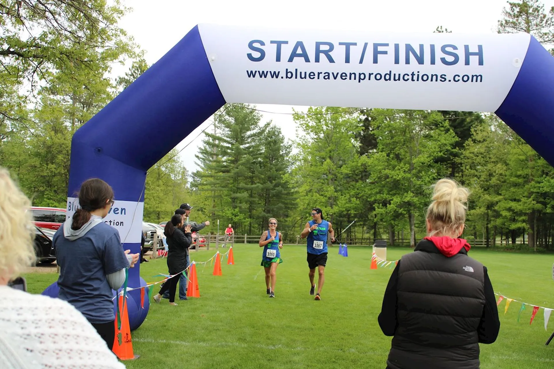 The image depicts an outdoor event where a few spectators are watching a runner crossing the