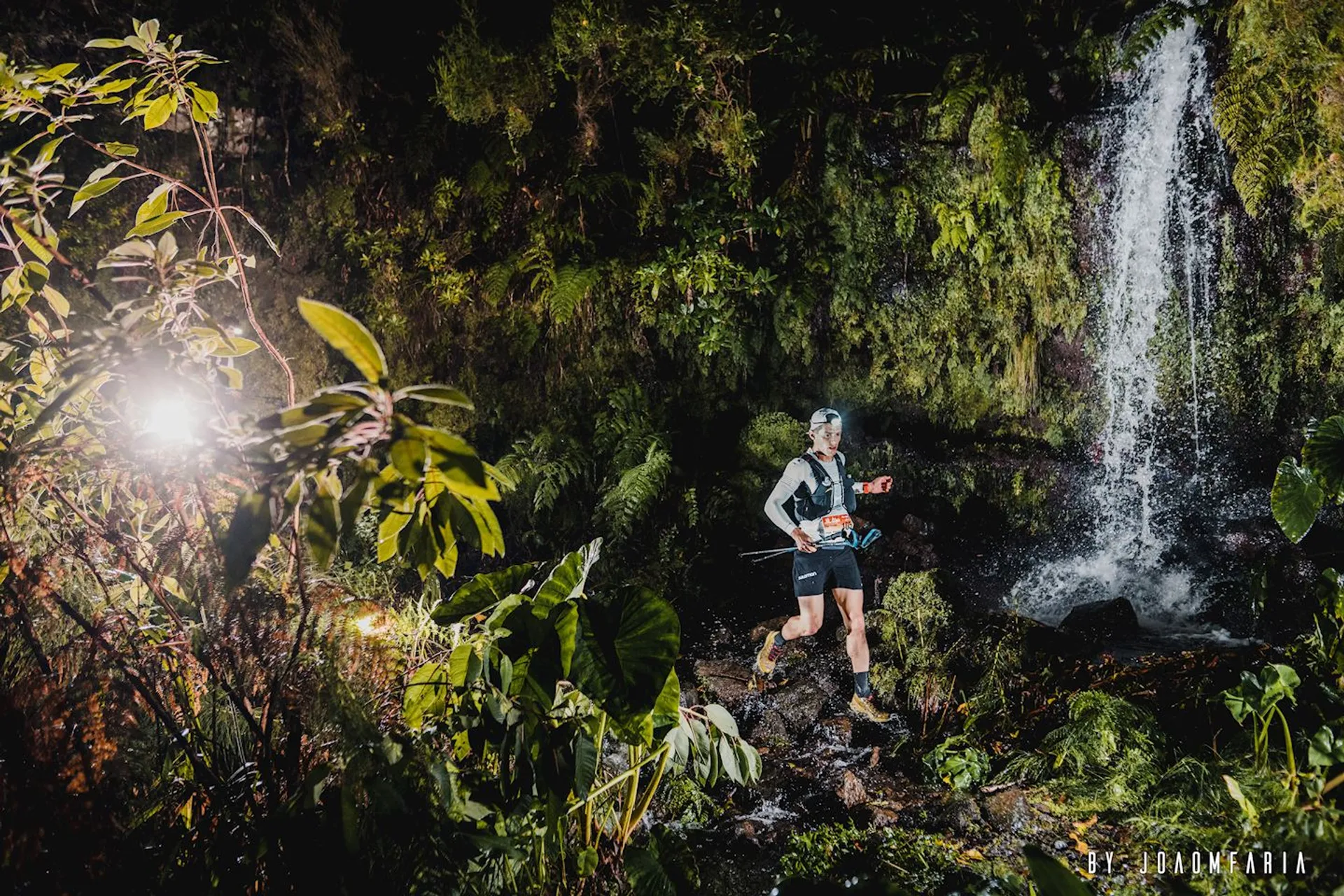 The image shows a nighttime scene where an individual is trail running through a lush,