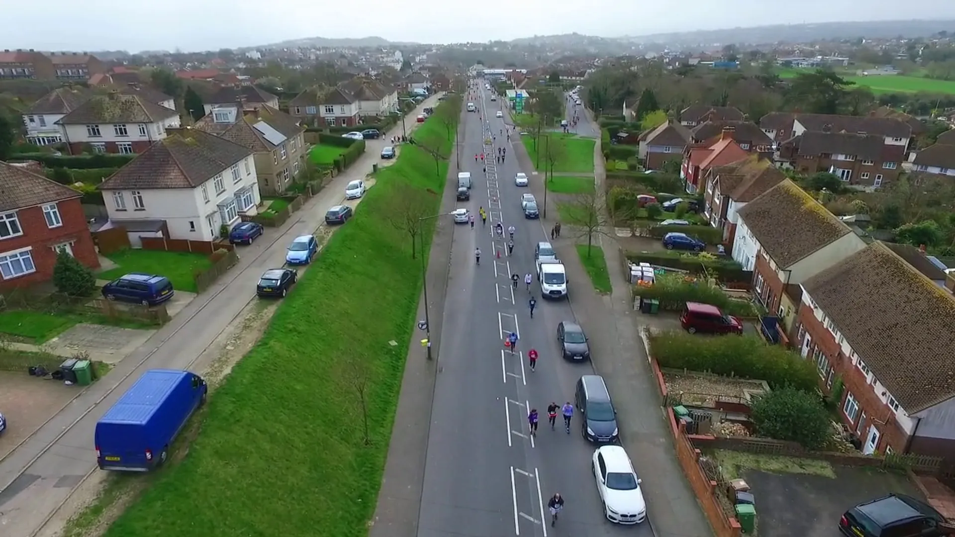 The image shows an aerial view of a wide street in a suburban area. There