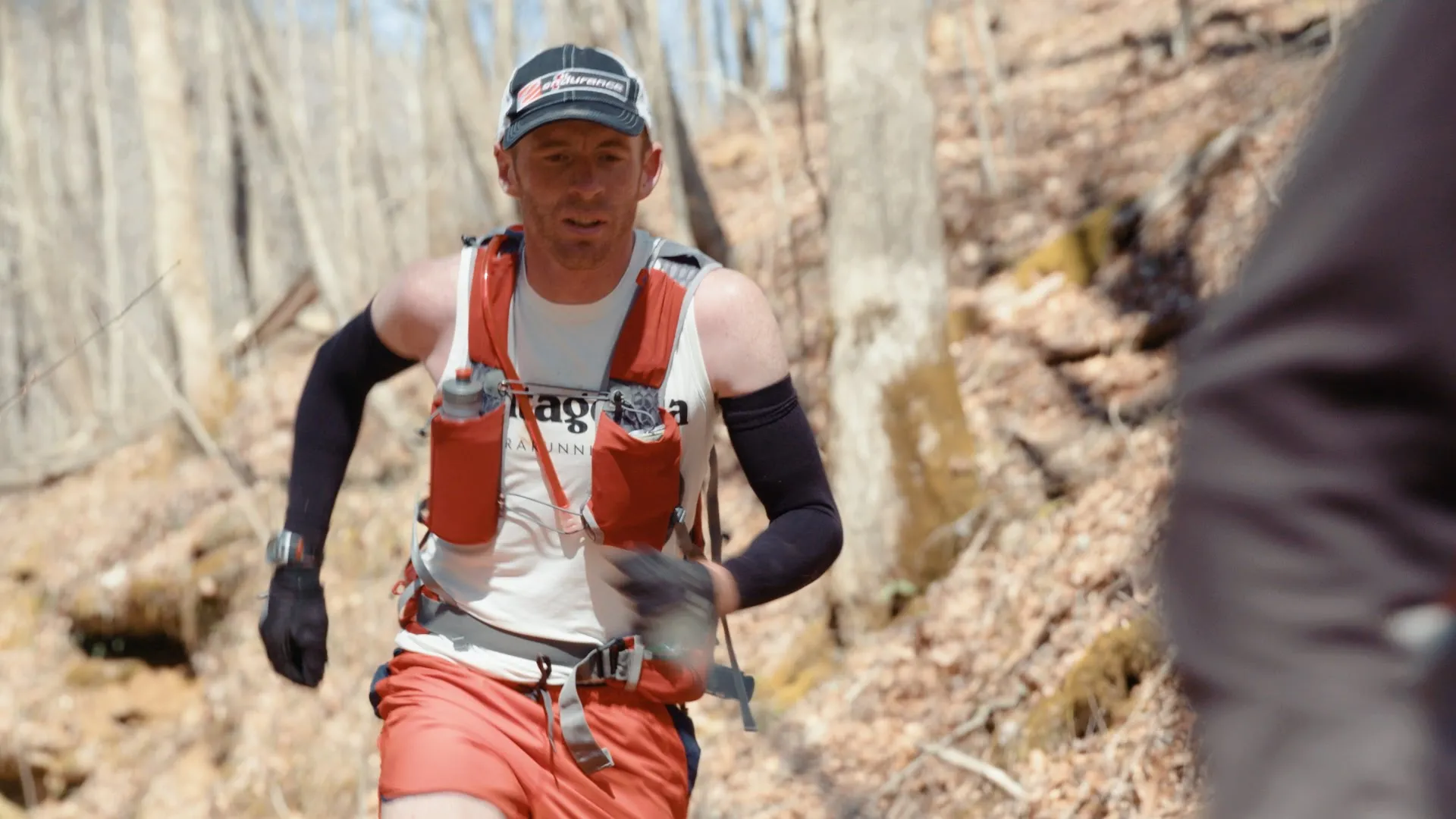 This image features a male runner in a trail running scenario. He's wearing a