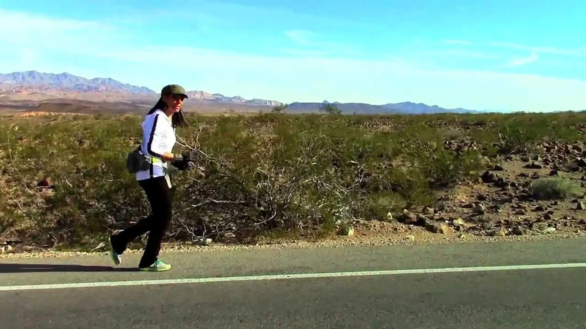 The image depicts a person walking or jogging alongside a road in a desert-like environment