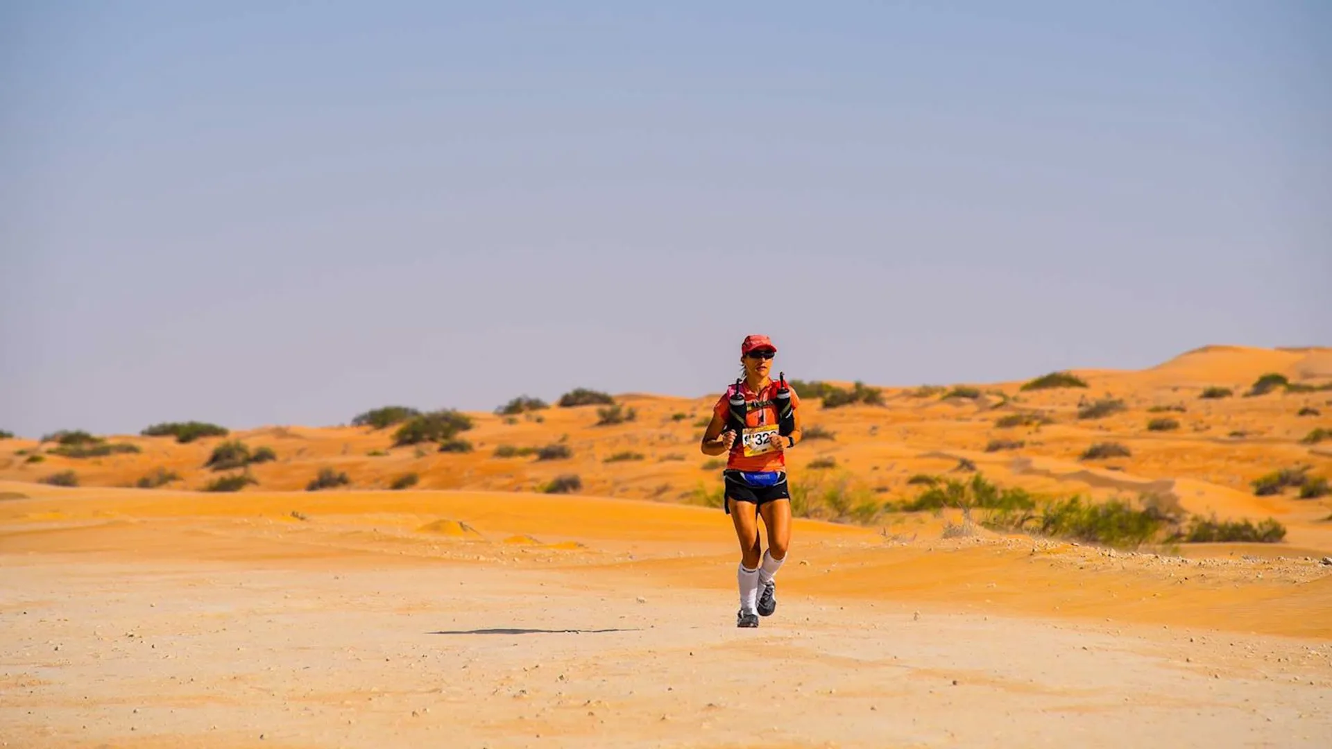 The image shows a person running in a desert environment. The runner is equipped with