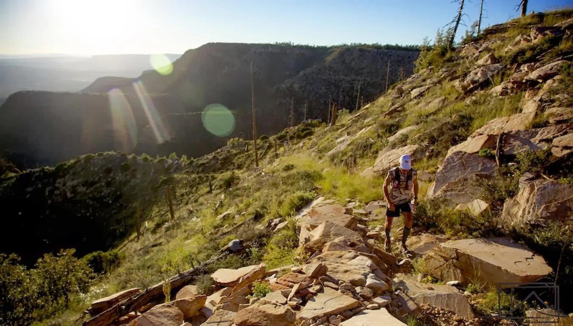 The image features a person hiking on a rocky trail in a mountainous area.
