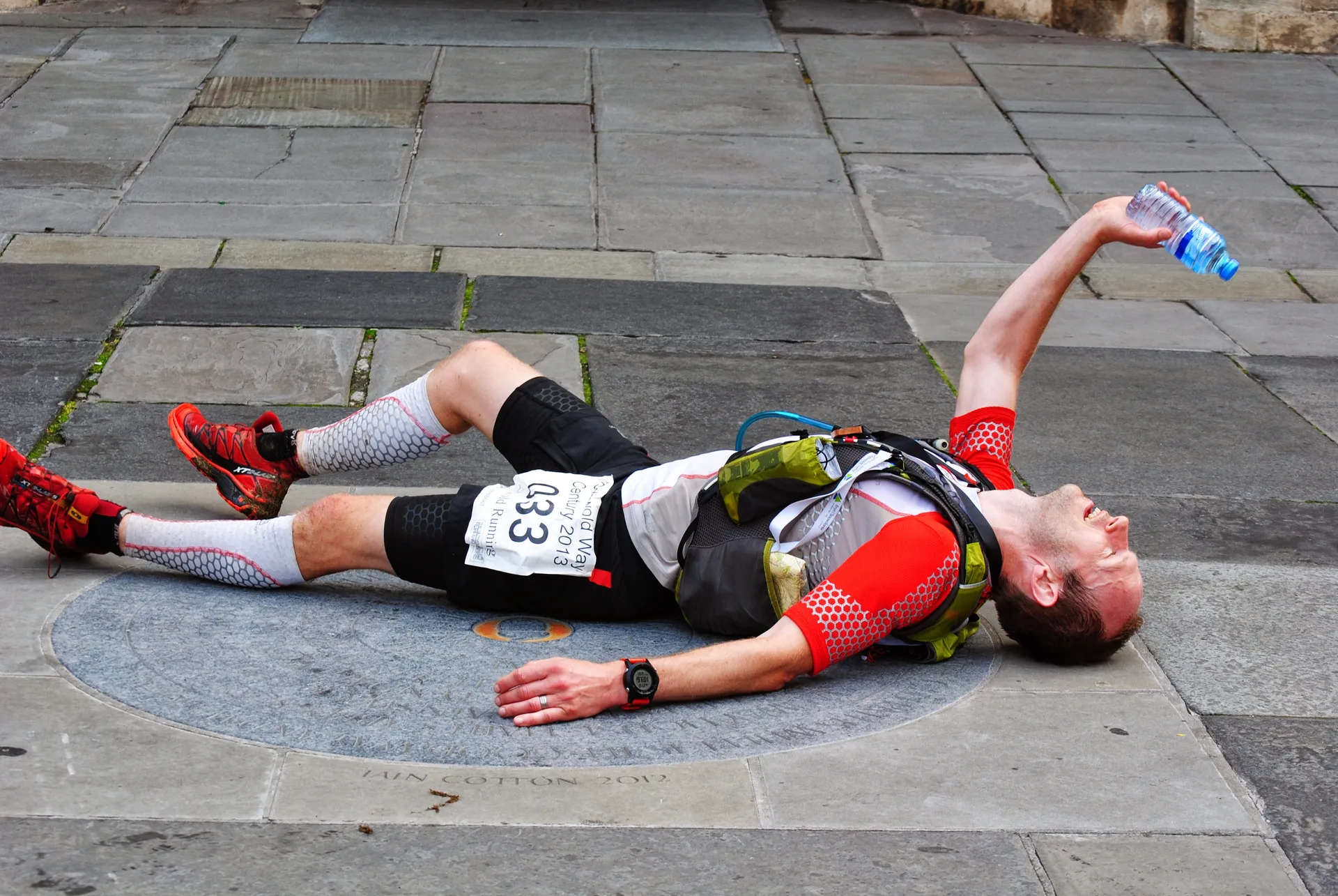 The image shows a person lying on their back on a stone pavement, possibly catching