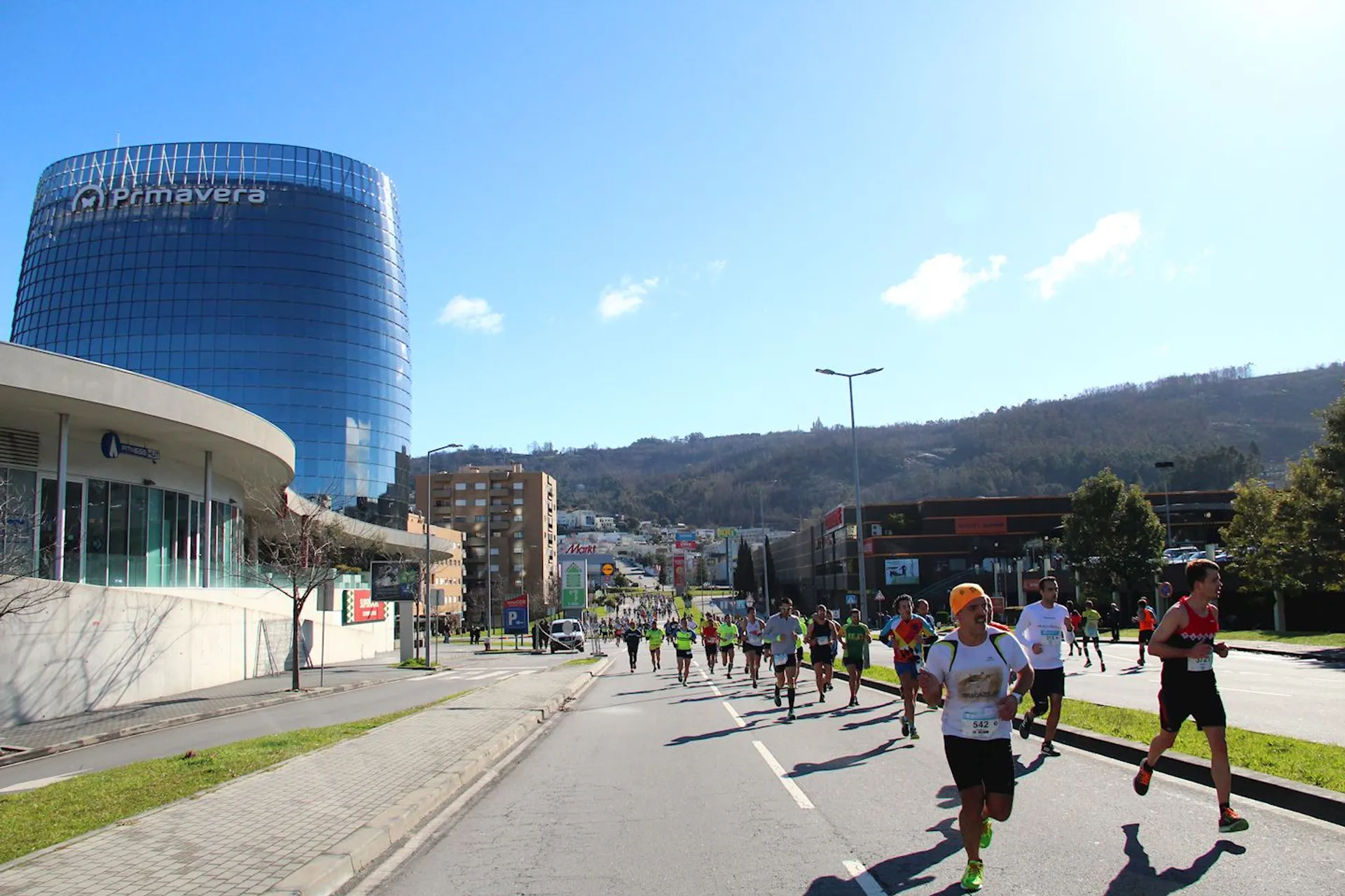 The image depicts a group of runners participating in a road race on a sunny day