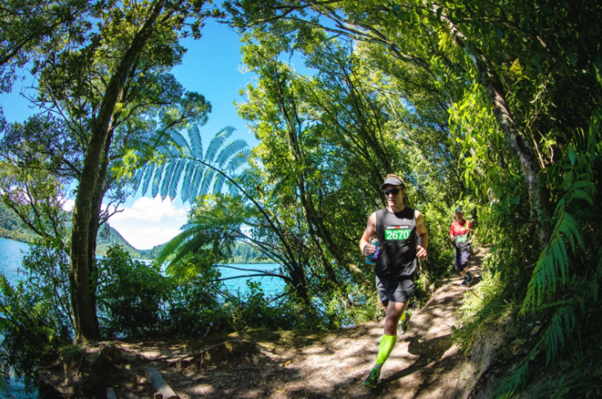 The image shows a trail running event in a lush, green natural environment. There
