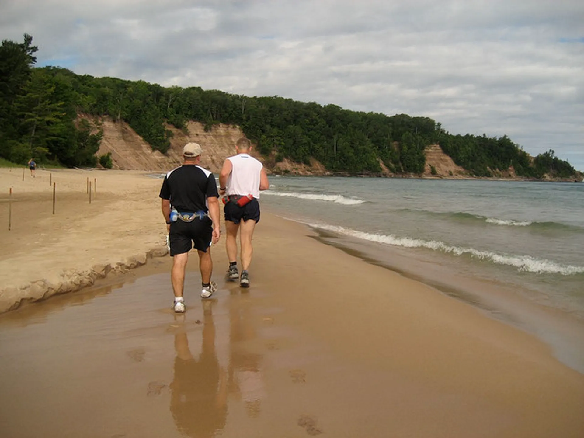 The image shows two people jogging along a sandy beach. They appear to be following