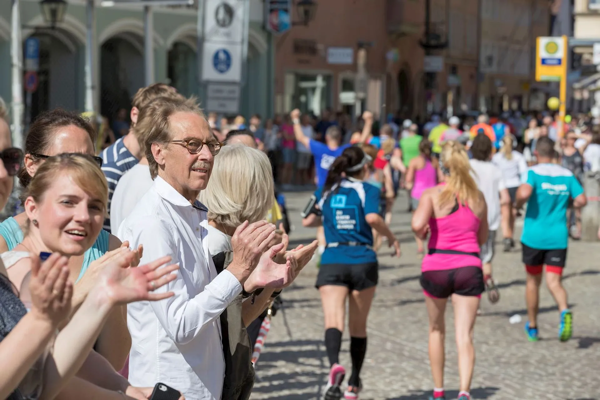The image depicts a group of spectators on the side of a street, clapping