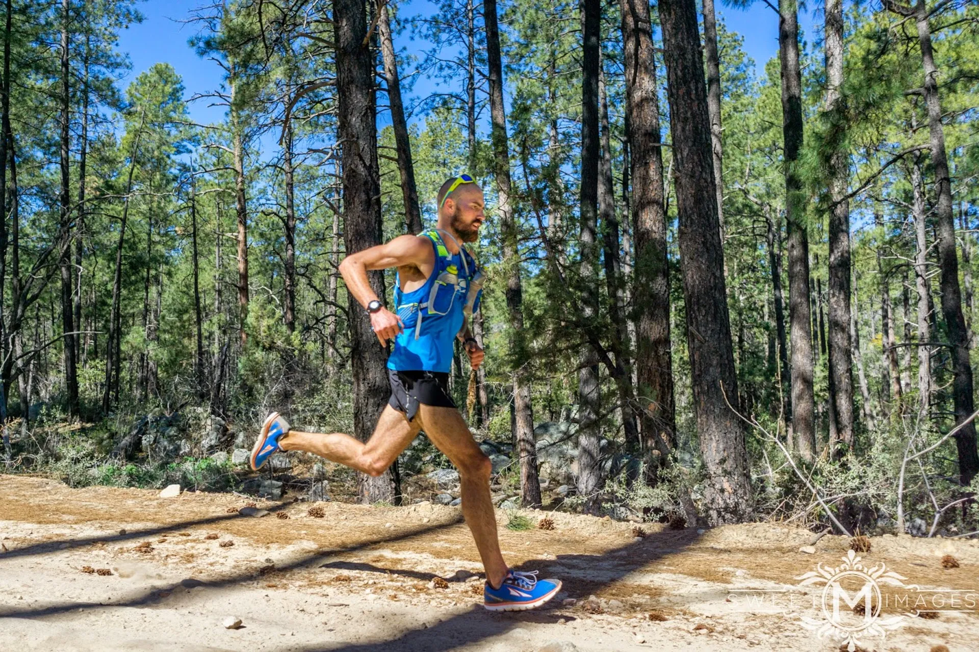 The image shows a man running through a forested area with tall pine trees.