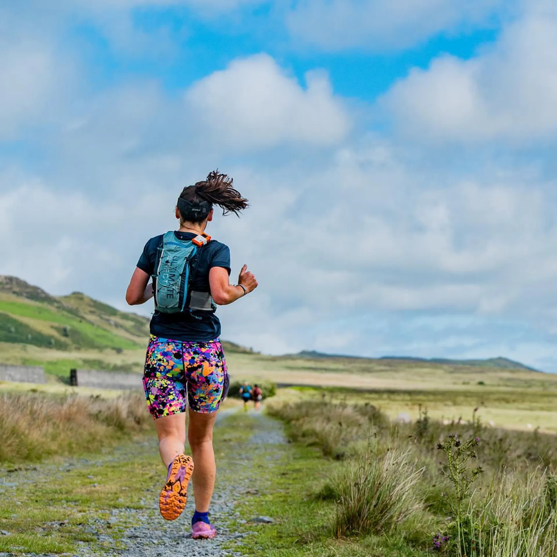The image shows a person running on a trail in a natural landscape. The runner