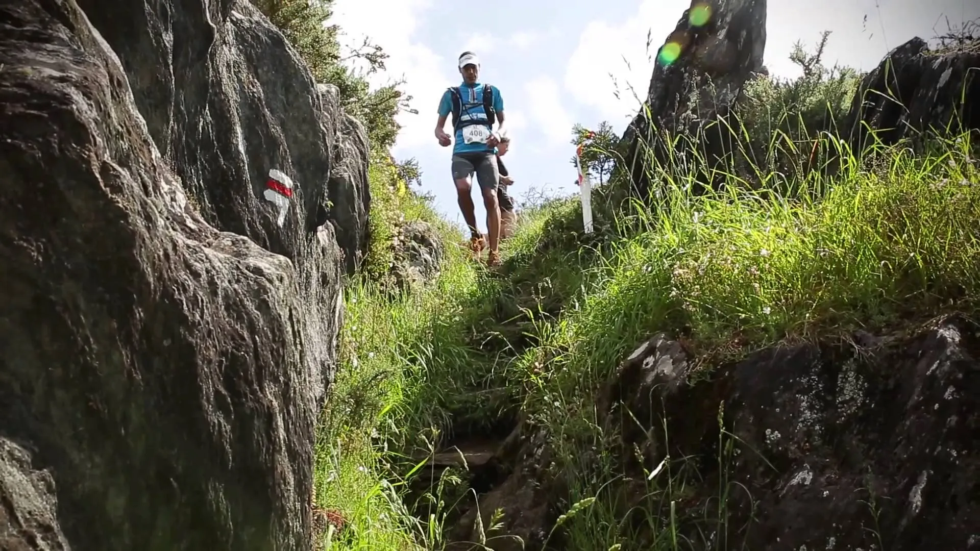 The image shows a person trail running or hiking on a narrow path between two rock