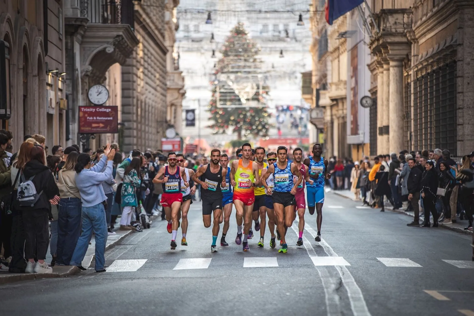 The image shows a group of runners competing in a road race, with spectators on