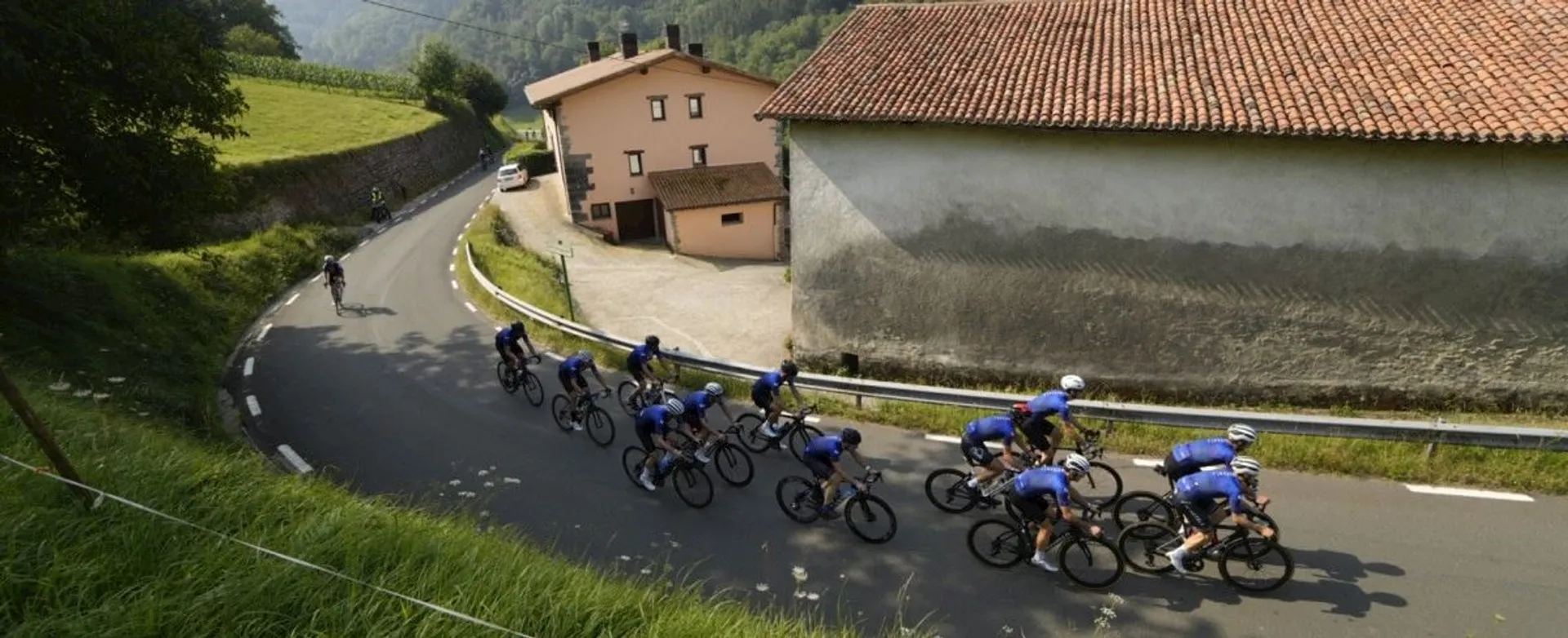 The image shows a group of cyclists riding on a winding road through a lush green