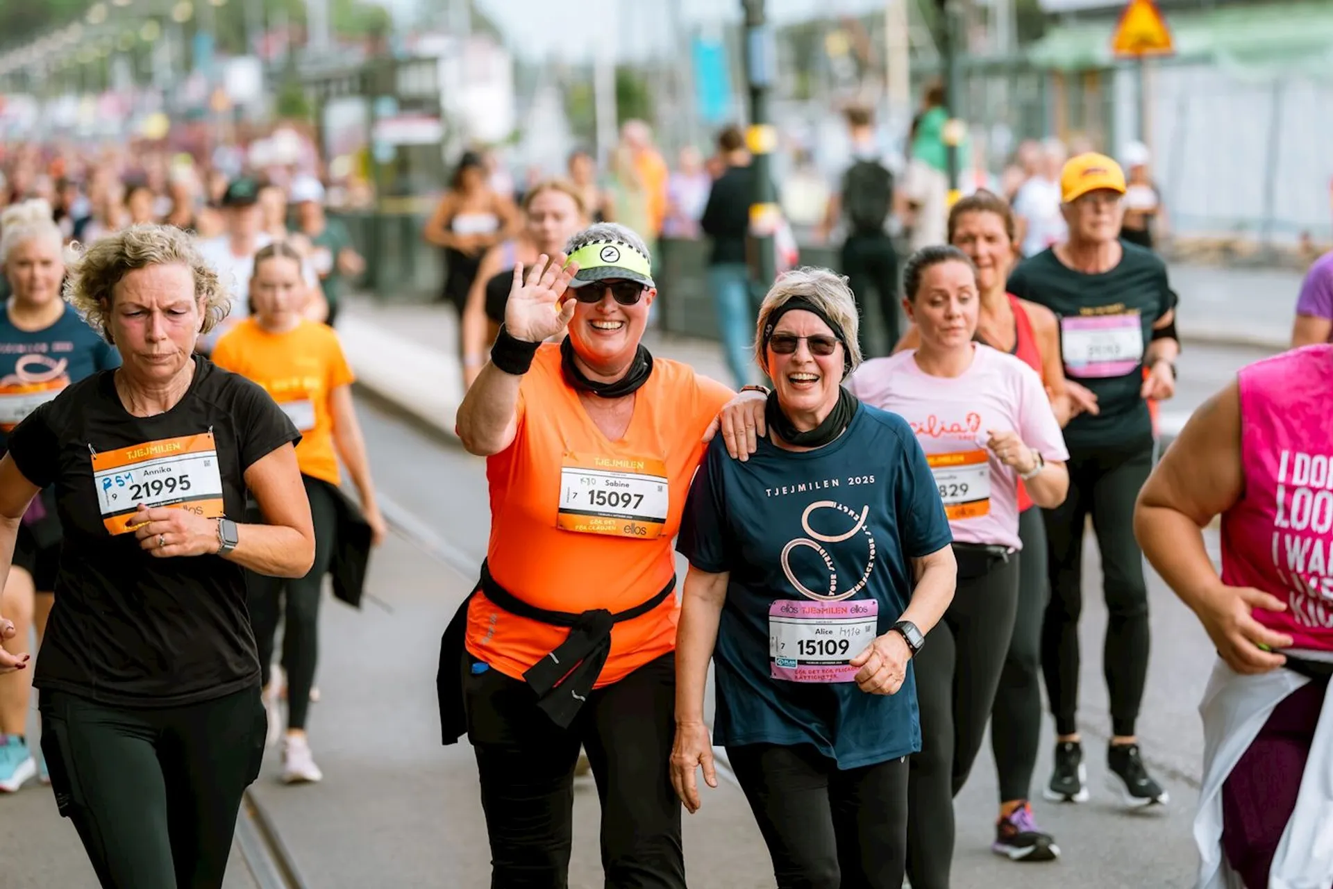 This image shows a group of people participating in a running event. They are wearing race bibs and athletic clothes, and some of them are smiling and waving at the camera. The image captures a lively atmosphere with multiple participants.