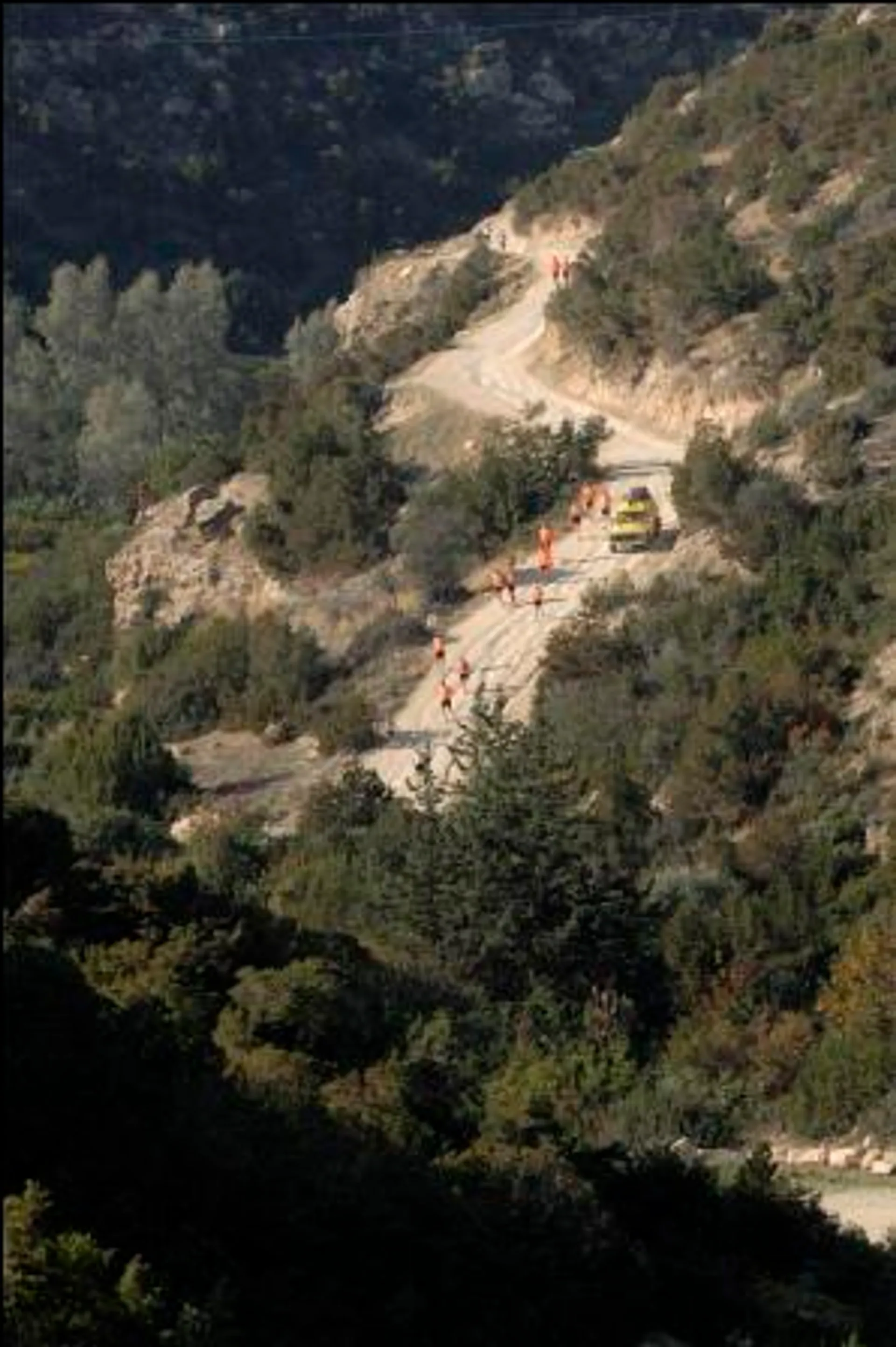 The image shows a winding mountain road or trail with several individuals walking along it.