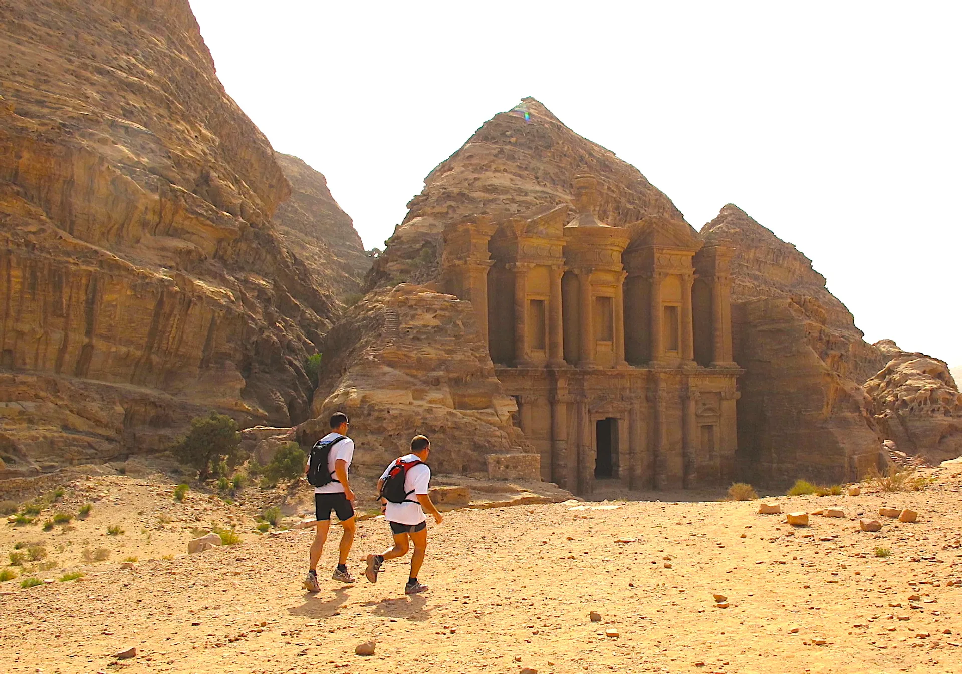 The image shows two individuals walking towards a large, ancient rock-cut structure with a