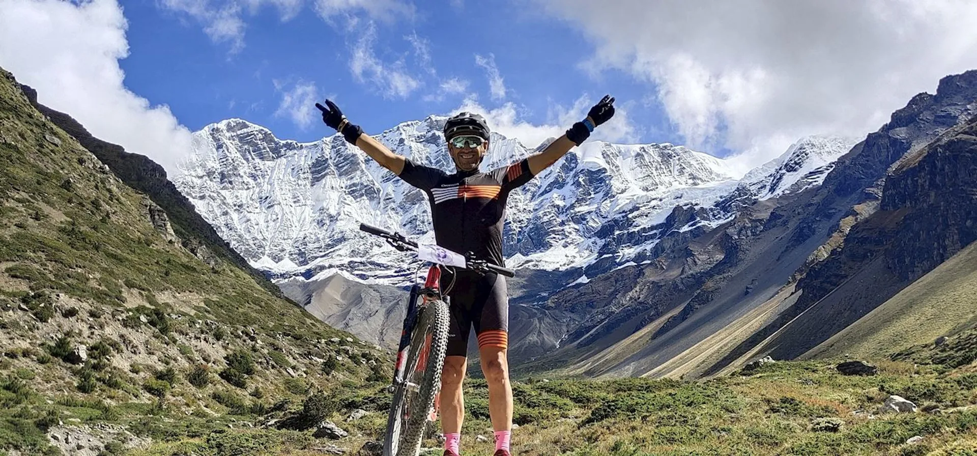 The image shows a person standing with a mountain bike amidst a mountainous landscape.