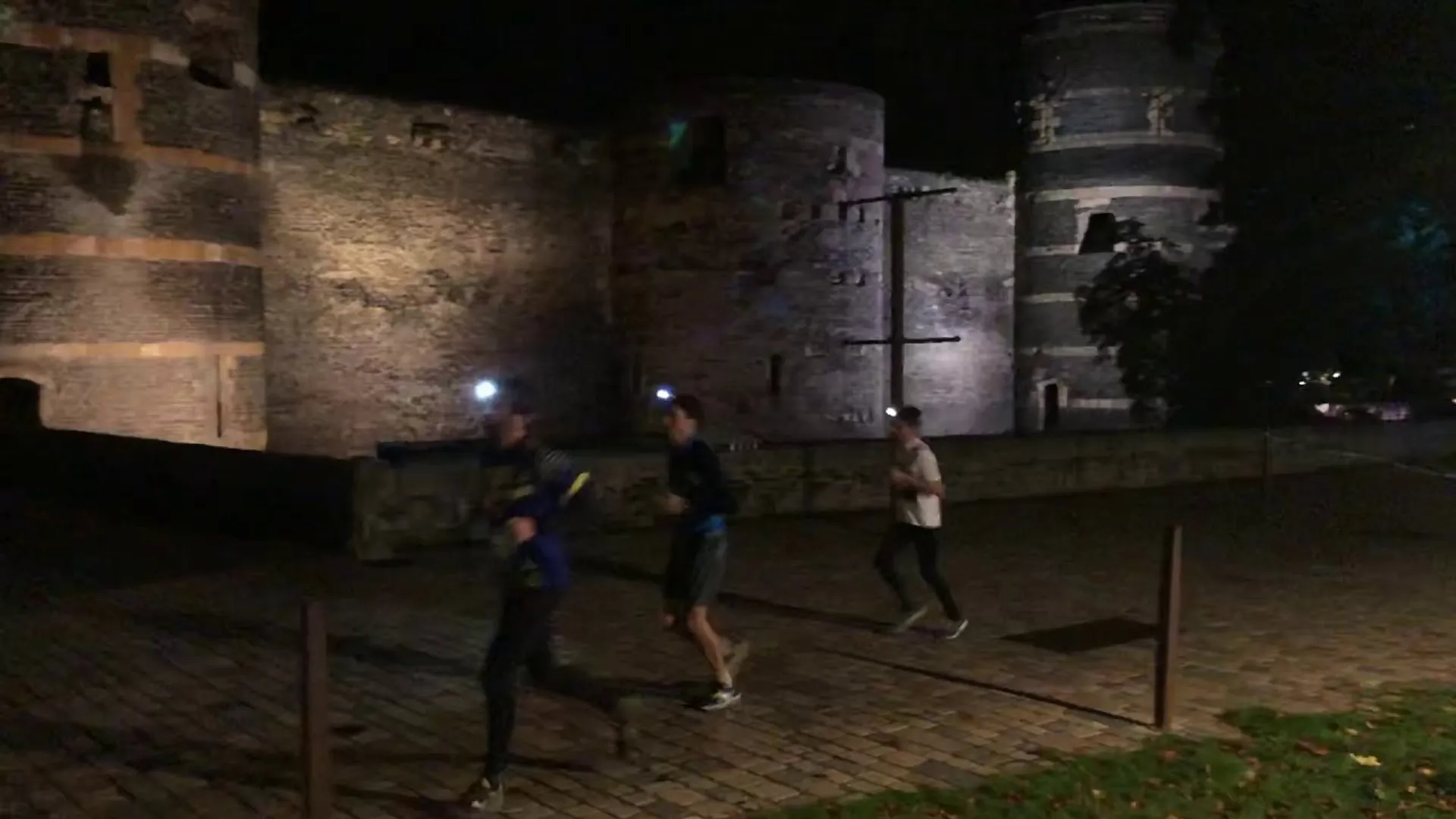 This image depicts three individuals running at night in front of an illuminated historical building,