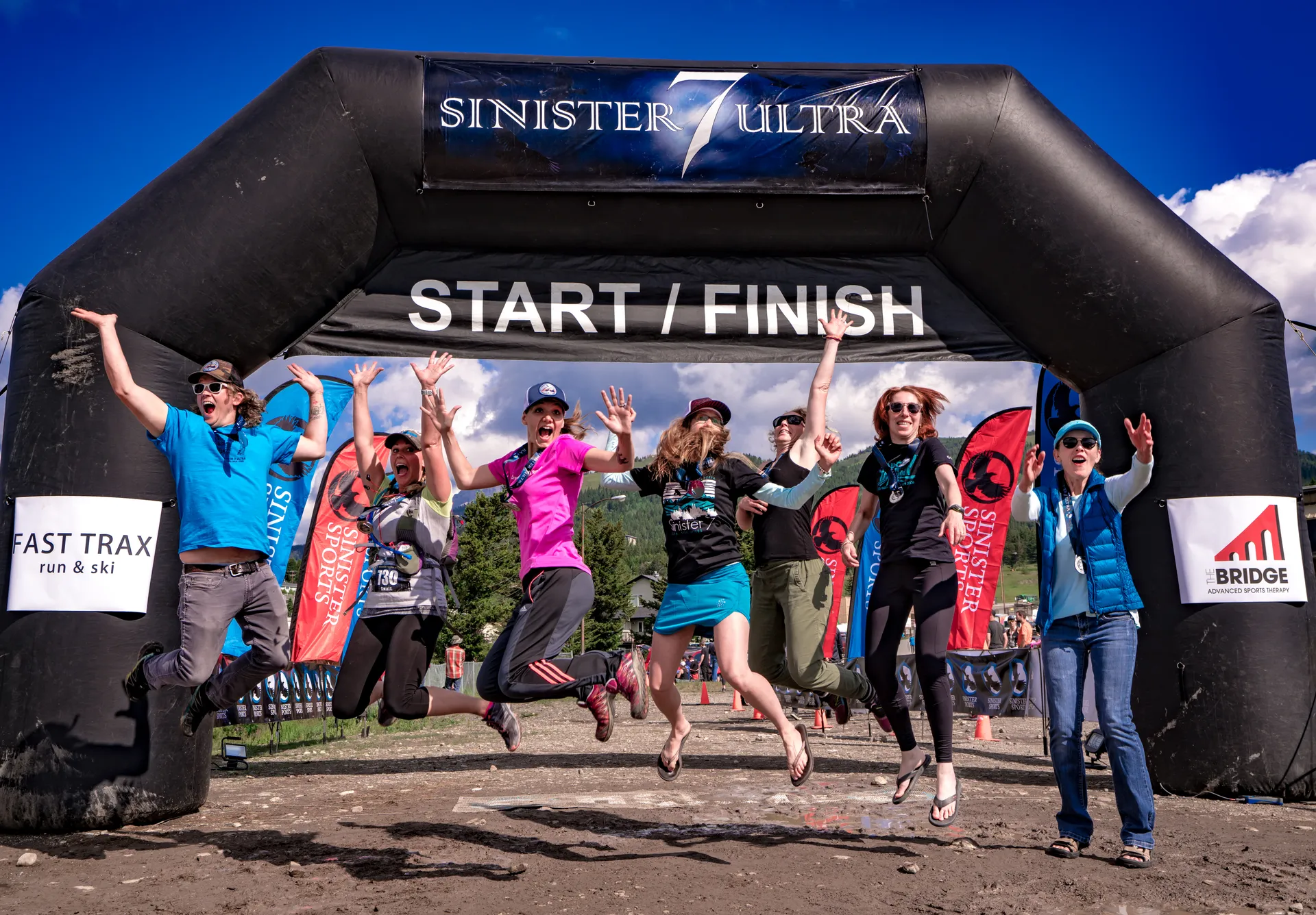 The image shows a group of people celebrating at a starting/finish line of a