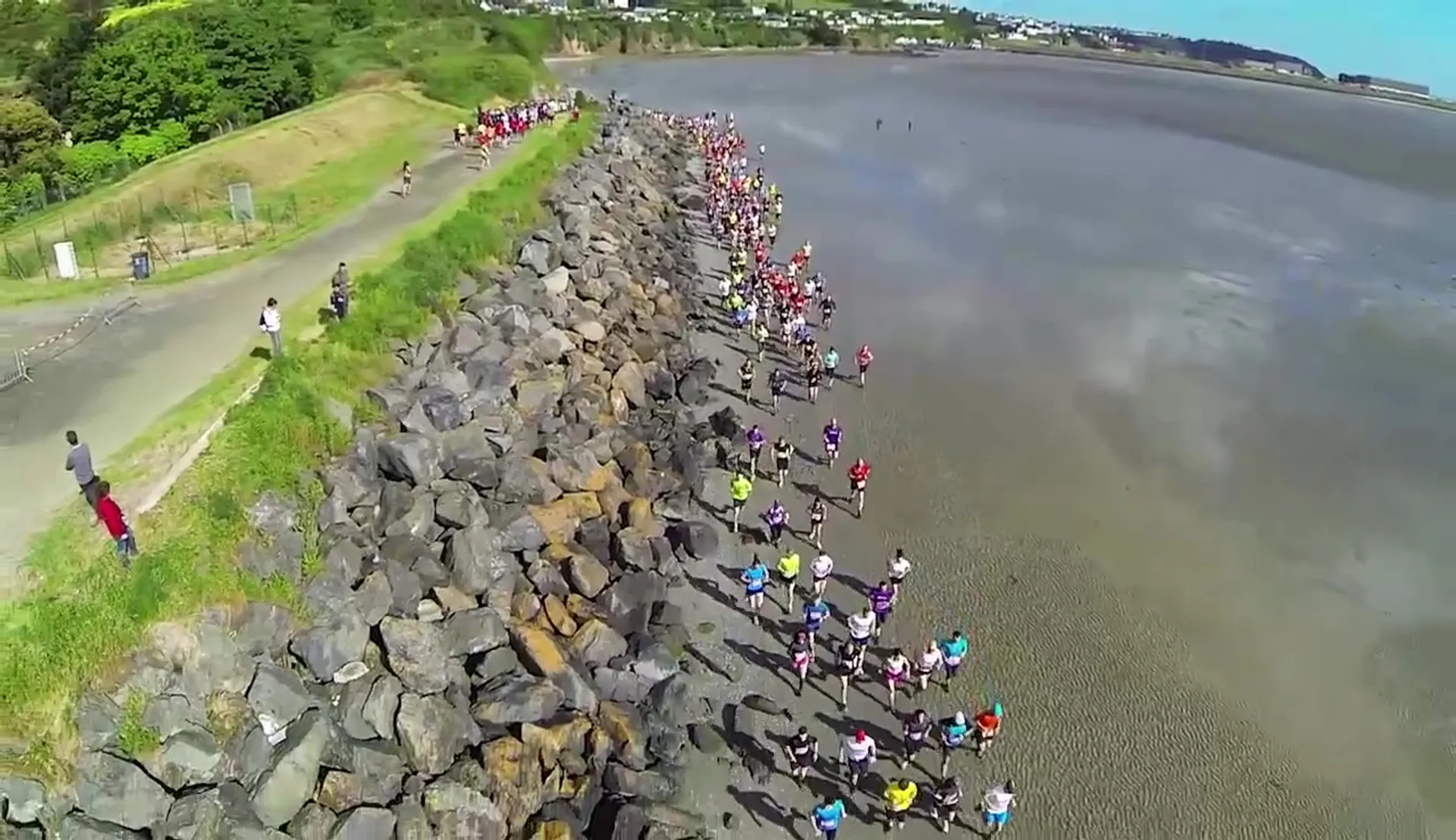 The image shows a group of people standing along a rocky coastline, possibly watching an