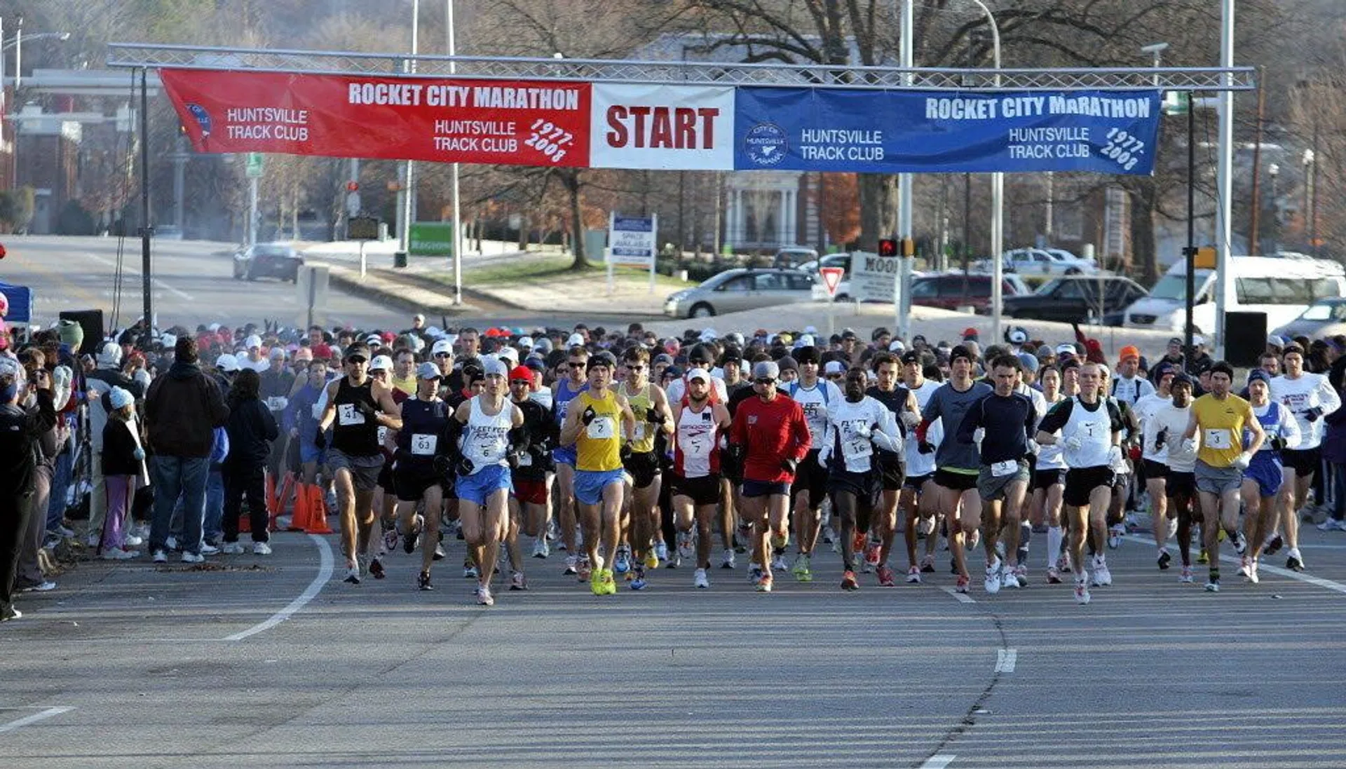 The image shows a group of runners at the start line of the Rocket City Marathon