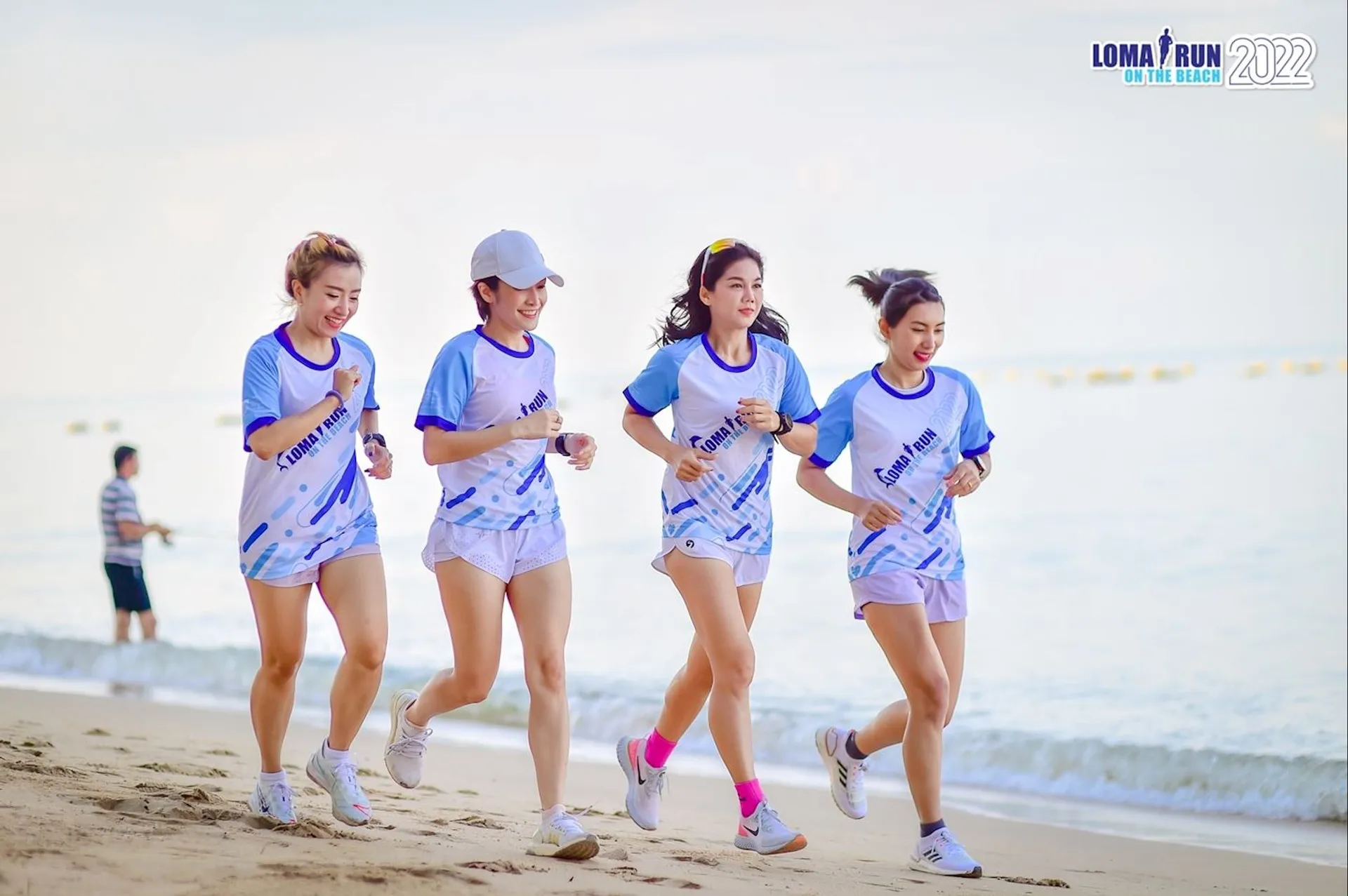The image shows four individuals participating in a fun run event on a beach, as