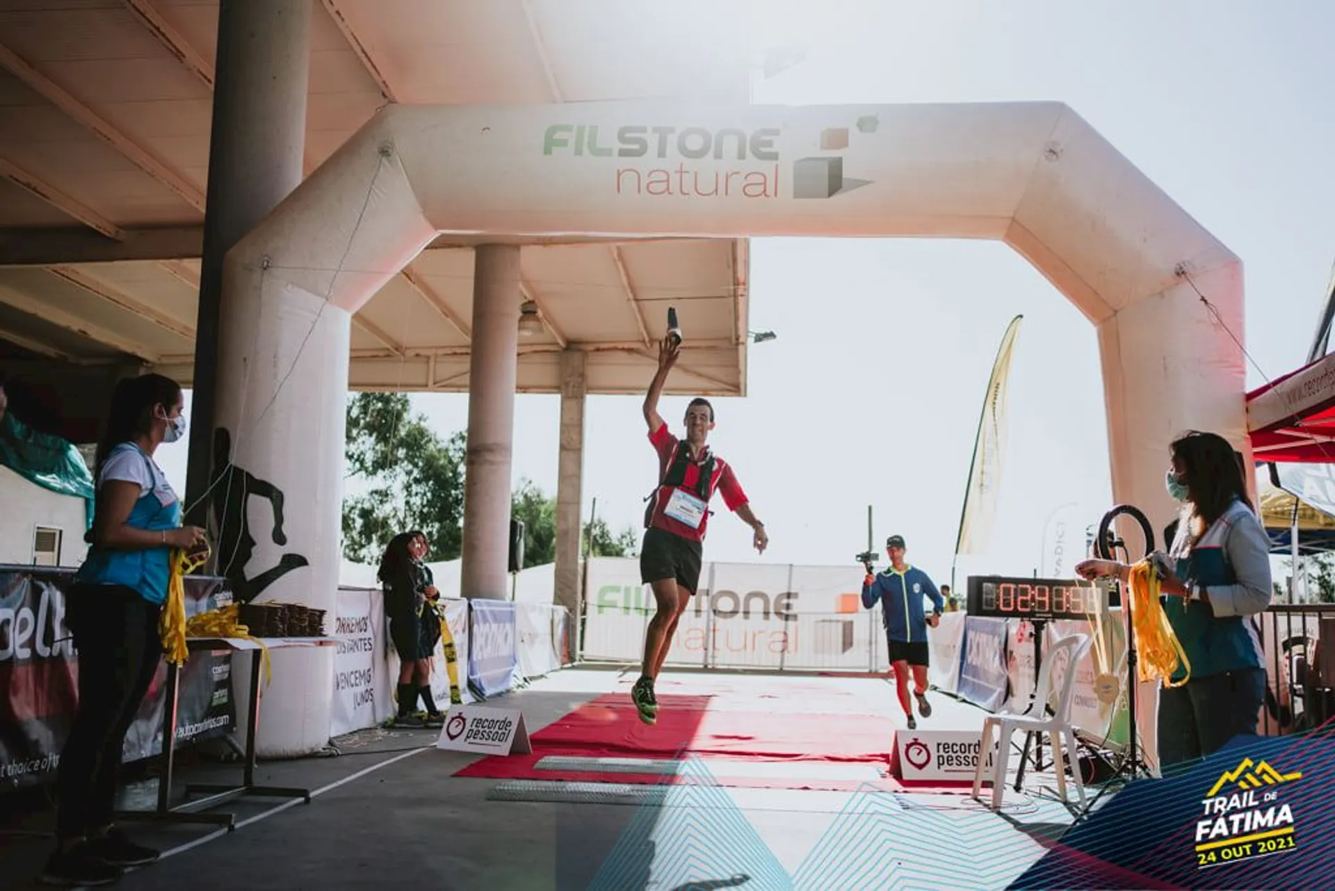 This image shows a runner crossing the finish line at a trail running event. The