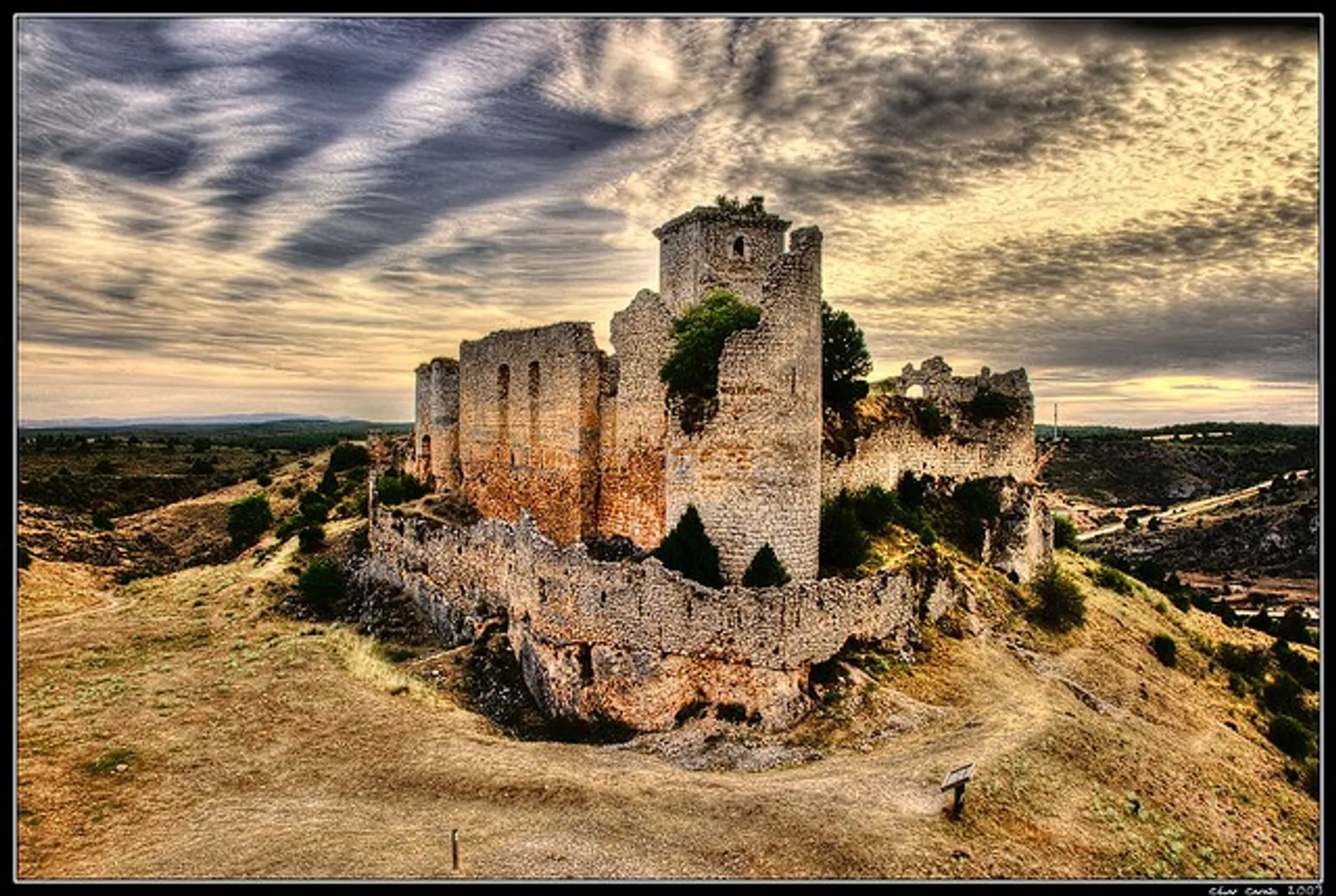 The image depicts a majestic, ruined castle sitting on elevated ground, most likely on