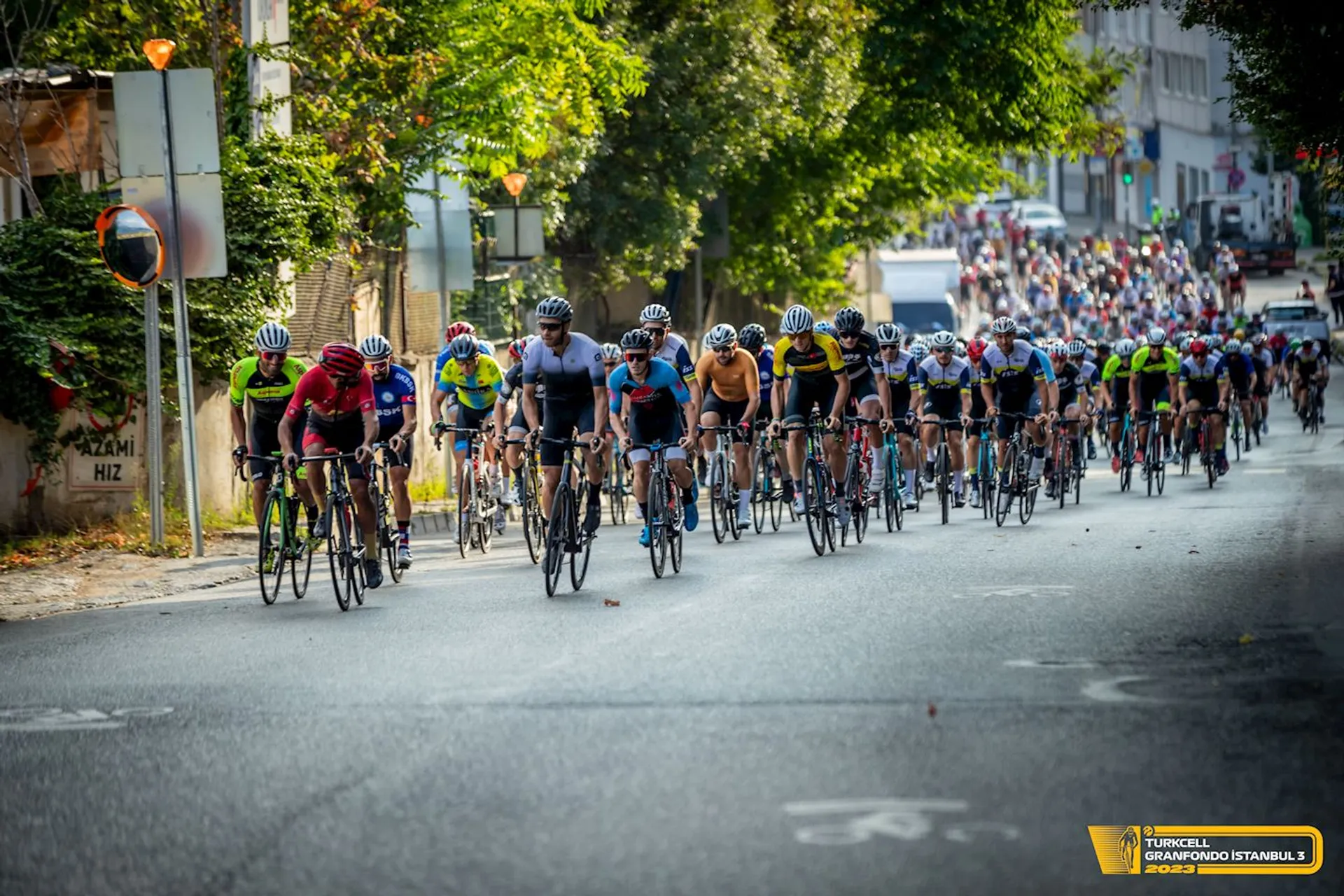 The image depicts a large group of cyclists participating in what appears to be a road